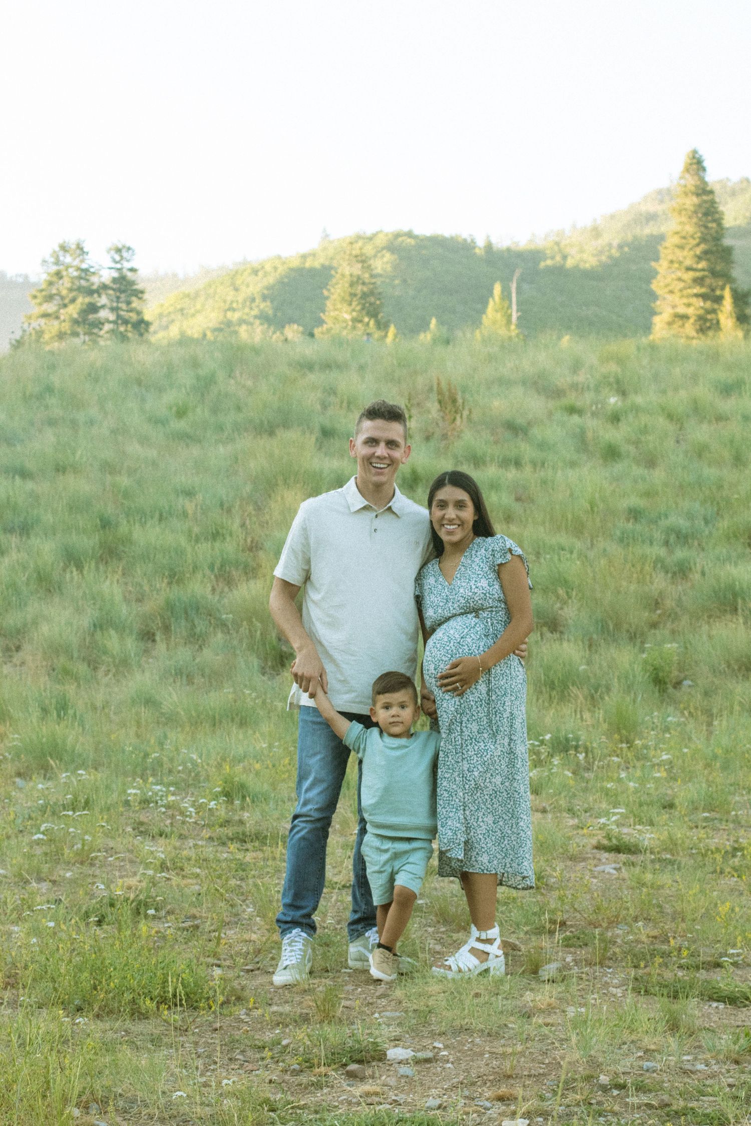 Family enjoying a sunny afternoon together on a grassy hillside during a summer photoshoot.