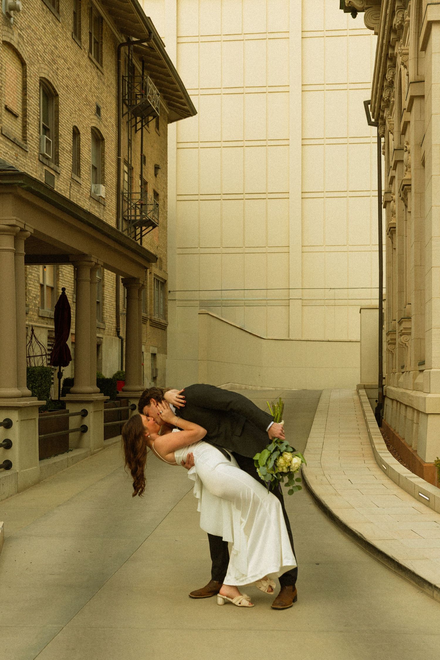 A romantic couple sharing a kiss in a curved hallway with elegant architecture and stone walls.