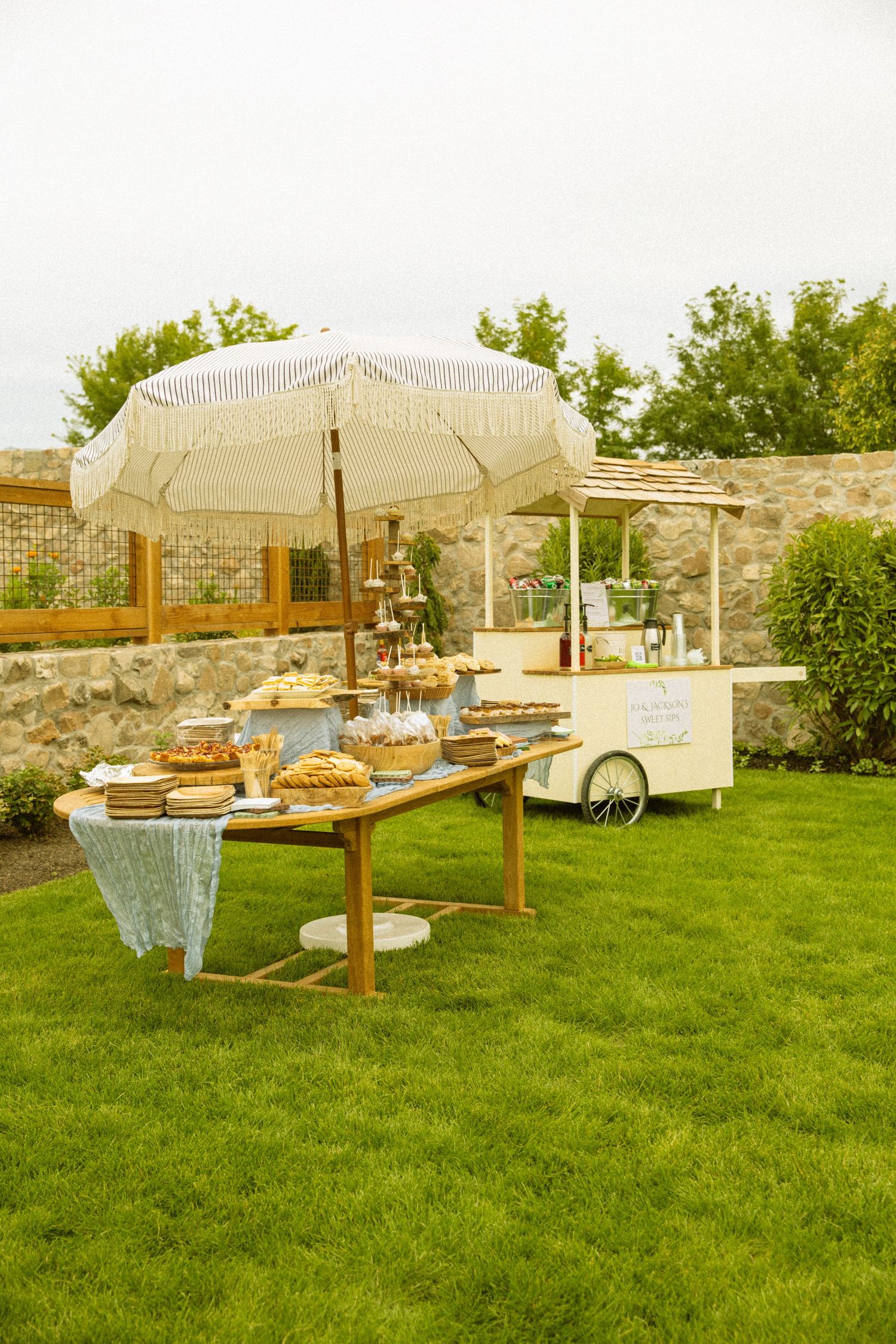 Outdoor wedding buffet setup with white umbrellas and wooden tables on grass.