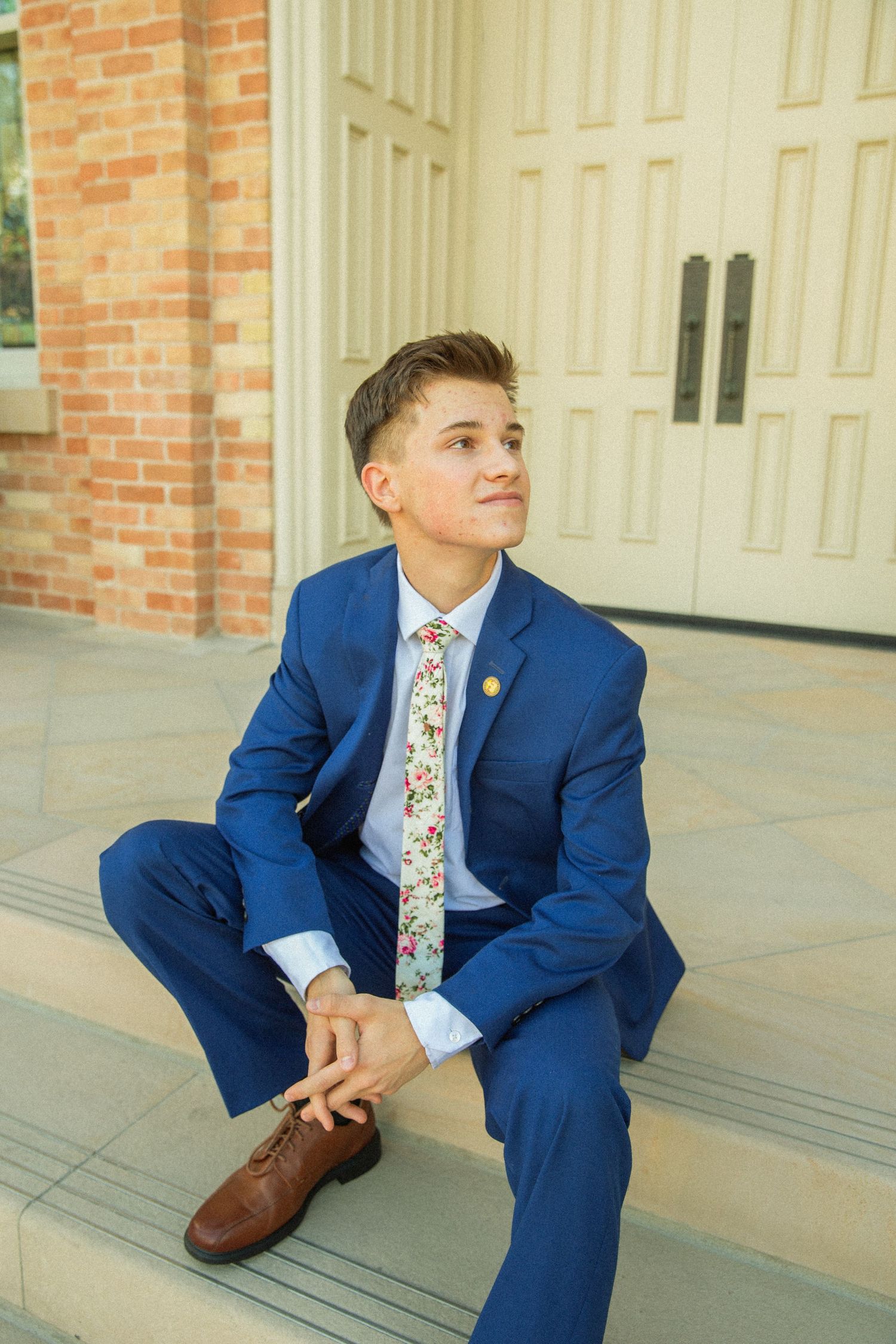 A person in a blue suit sits thoughtfully on outdoor steps against a brick and white column backdrop.