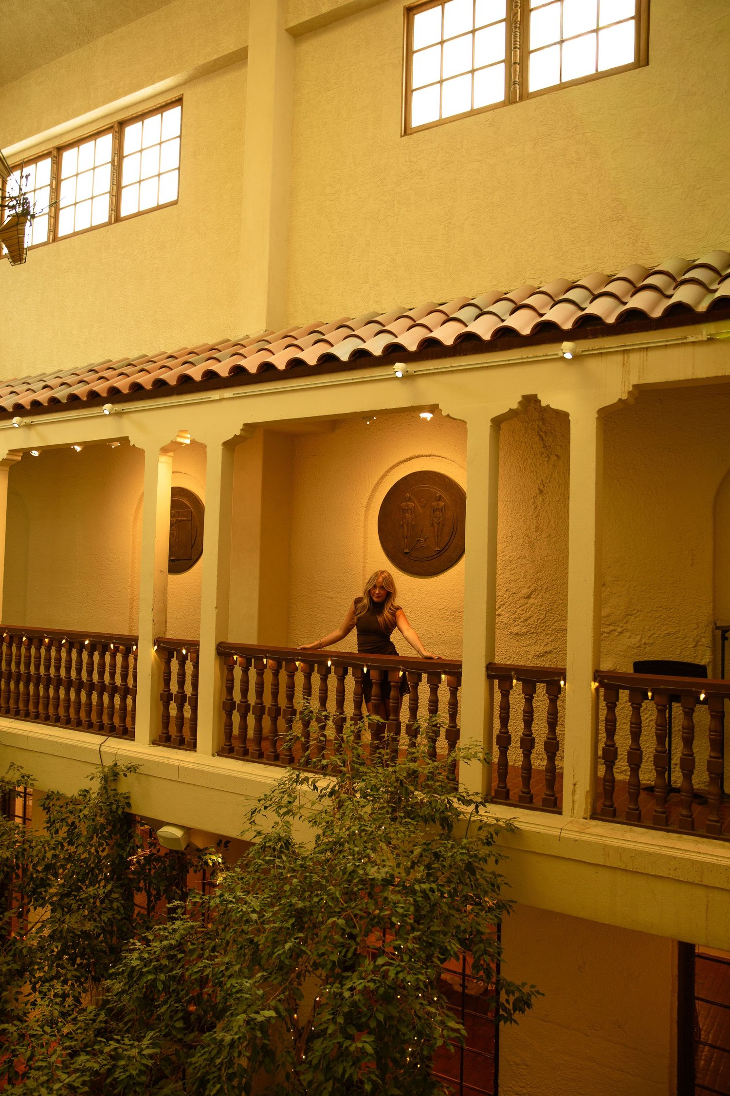 Woman standing on a balcony of a Spanish colonial-style building with terracotta roof tiles and ornate railings.
