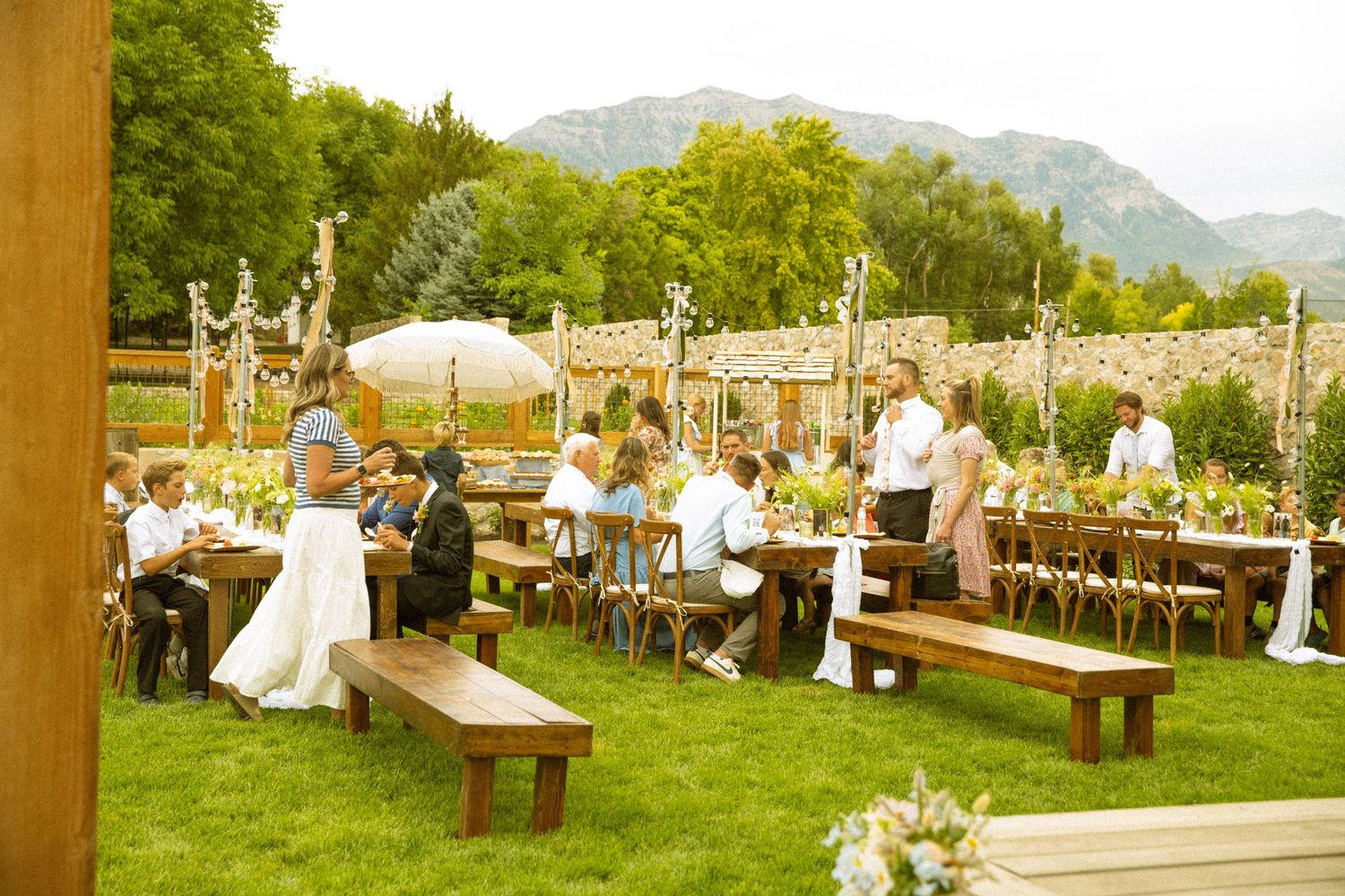 Outdoor wedding reception setup with long wooden tables and mountain backdrop.