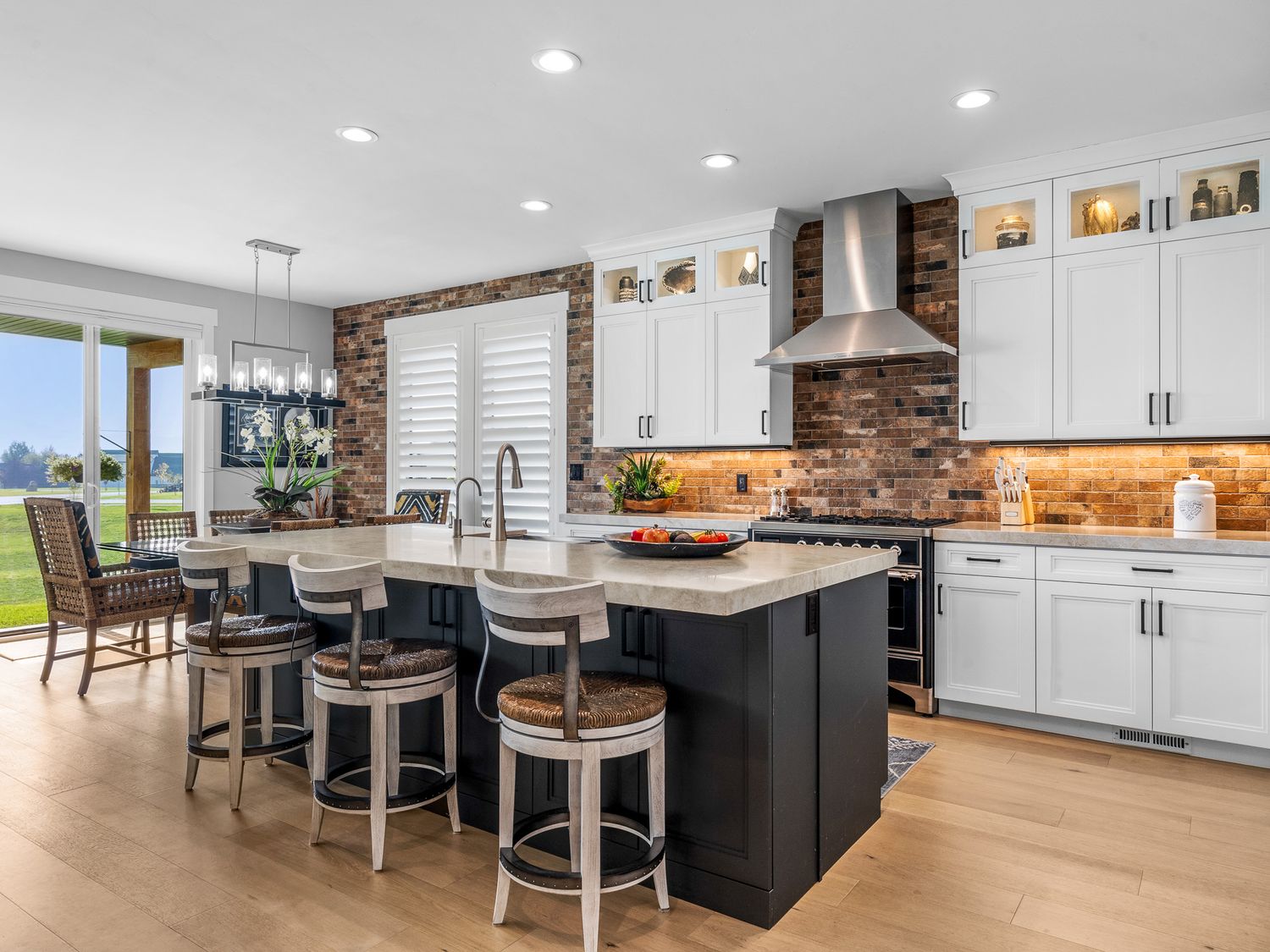 Spacious kitchen with white cabinets, black island, brick backsplash, wall-mount hood, and hardwood floors.