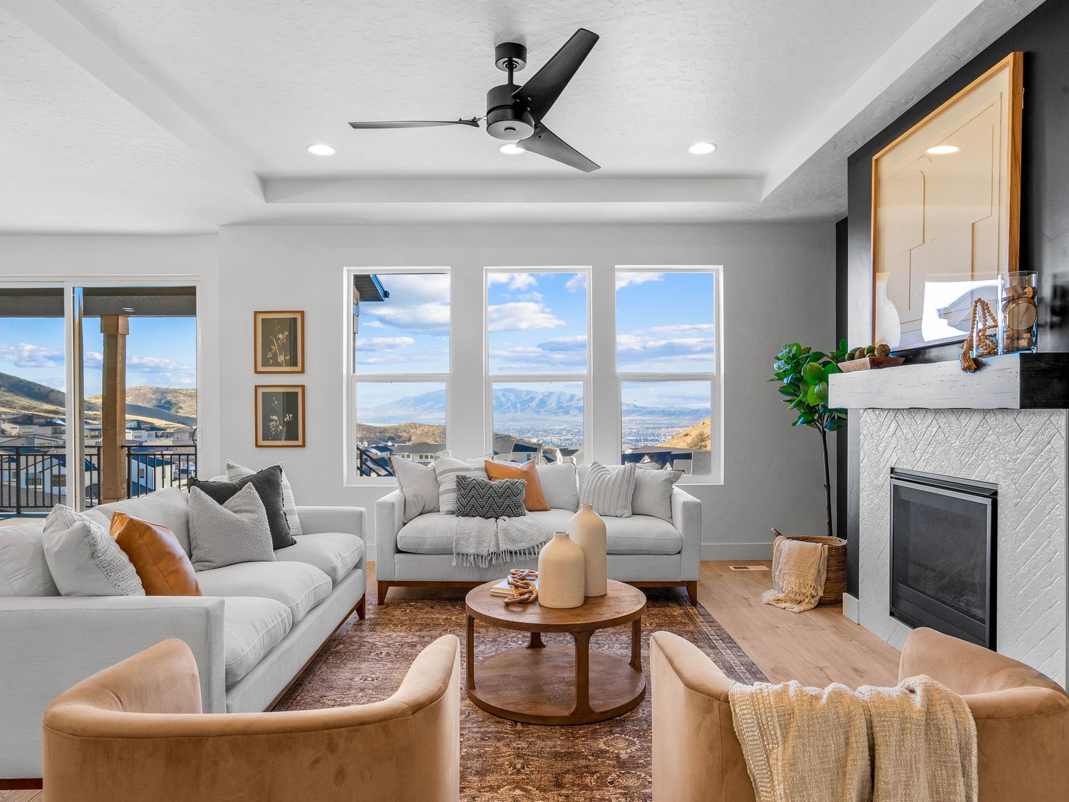 Bright living room with tray ceiling, fireplace, large windows, and stunning lake and mountain views.