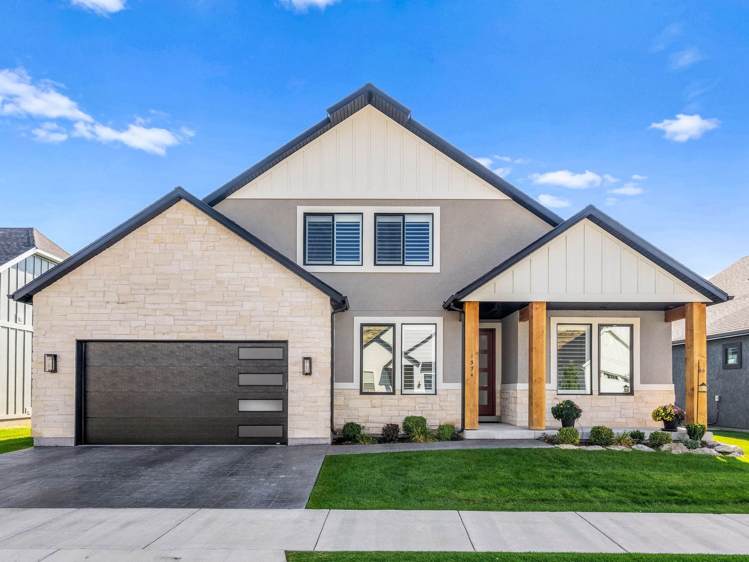 Modern craftsman home with stone accents, dark garage door, and manicured lawn under blue sky.