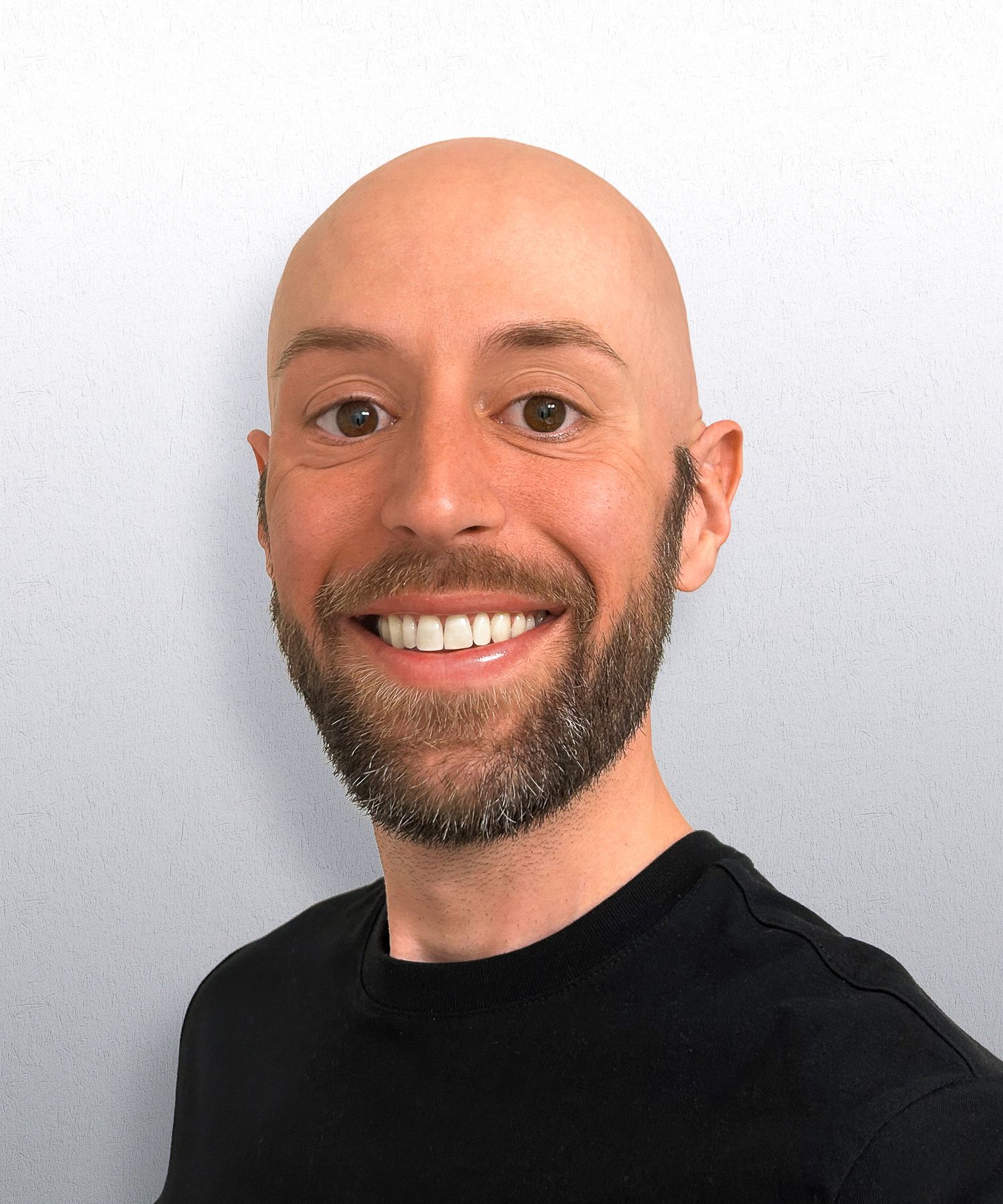 Smiling bald man with a beard wearing a black shirt against a light gray background.