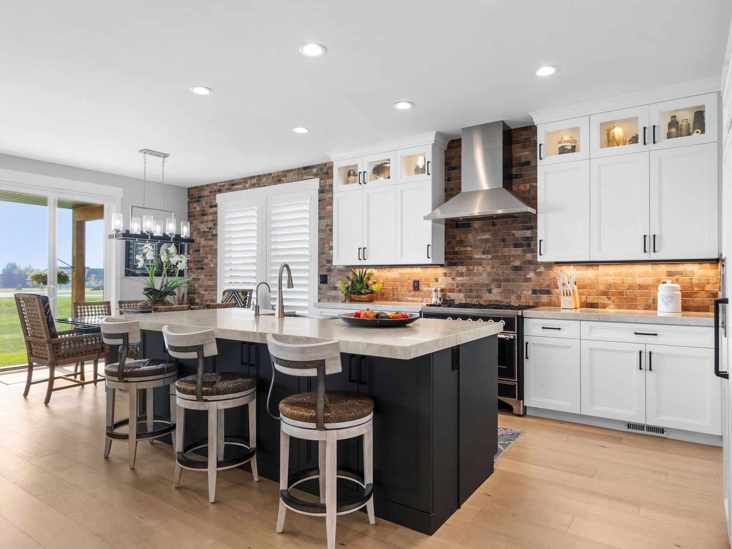 Modern kitchen with black island, white shaker cabinets, brick backsplash, and light hardwood floors.