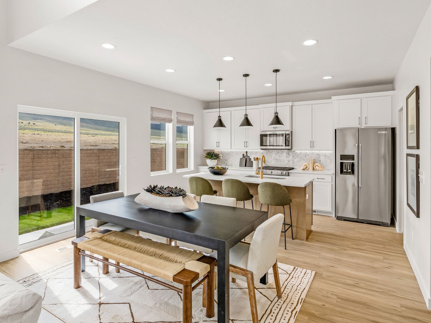 Bright open-concept dining and kitchen area with white cabinets, pendant lights, and sliding glass doors.