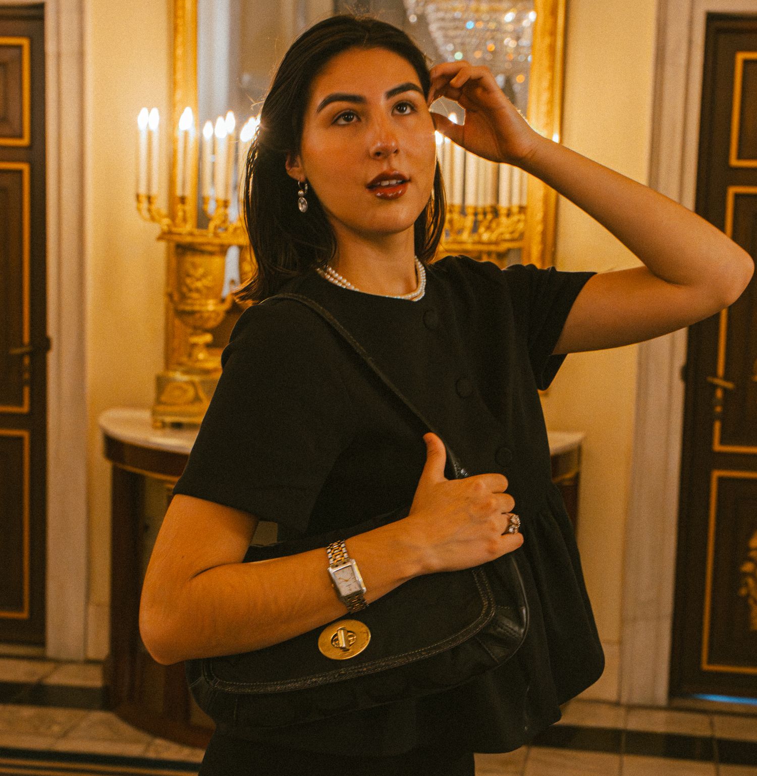 A woman looks dreamy in the Amsterdam palace holding a bag and wearing tasteful jewelry.