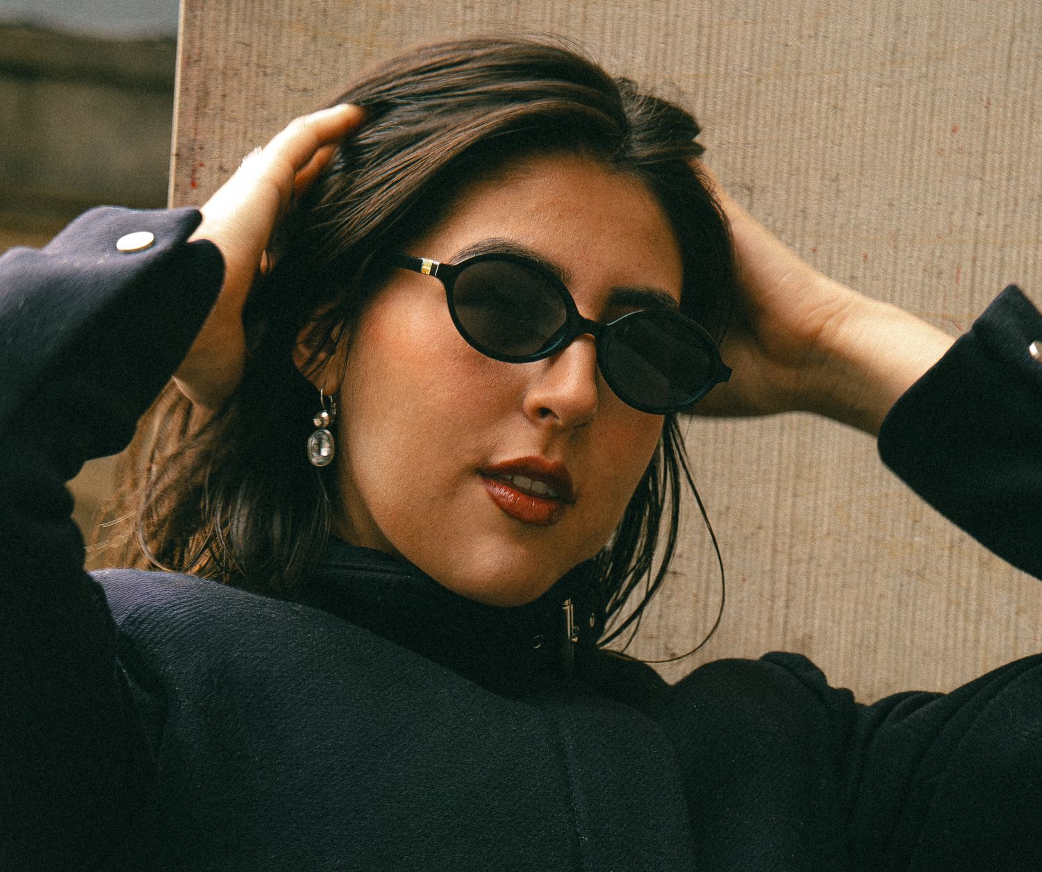 A woman looks confidently into the camera wearing black sunglasses.