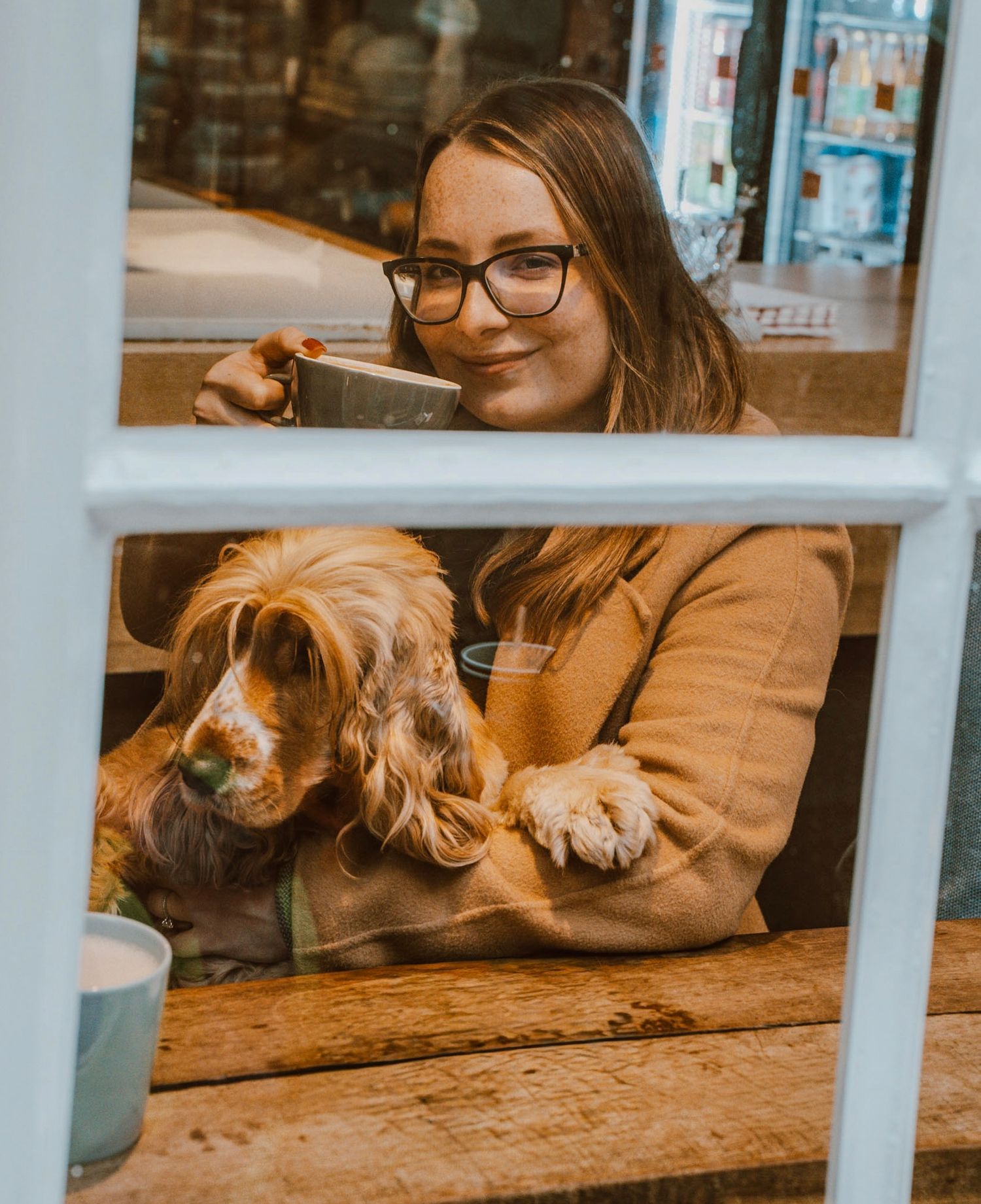 Girl is romantically sipping coffee in a cafe with her pet in her lap.