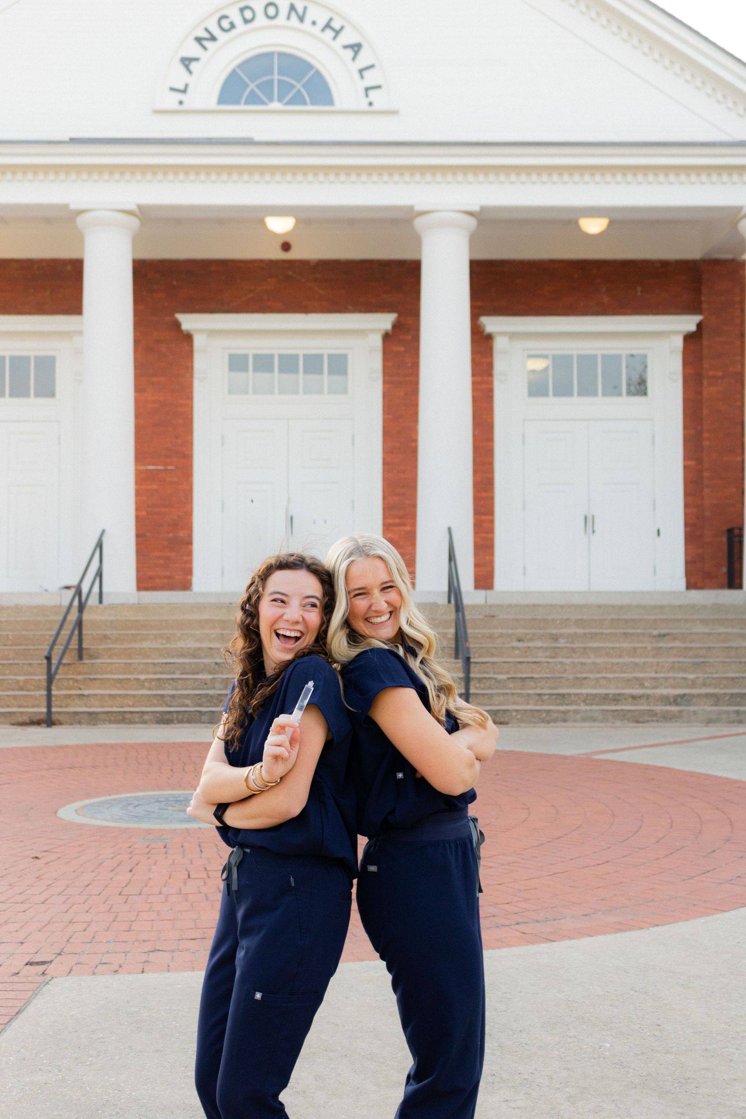 Two friends in navy uniforms pose back-to-back in front of Langdon Hall.