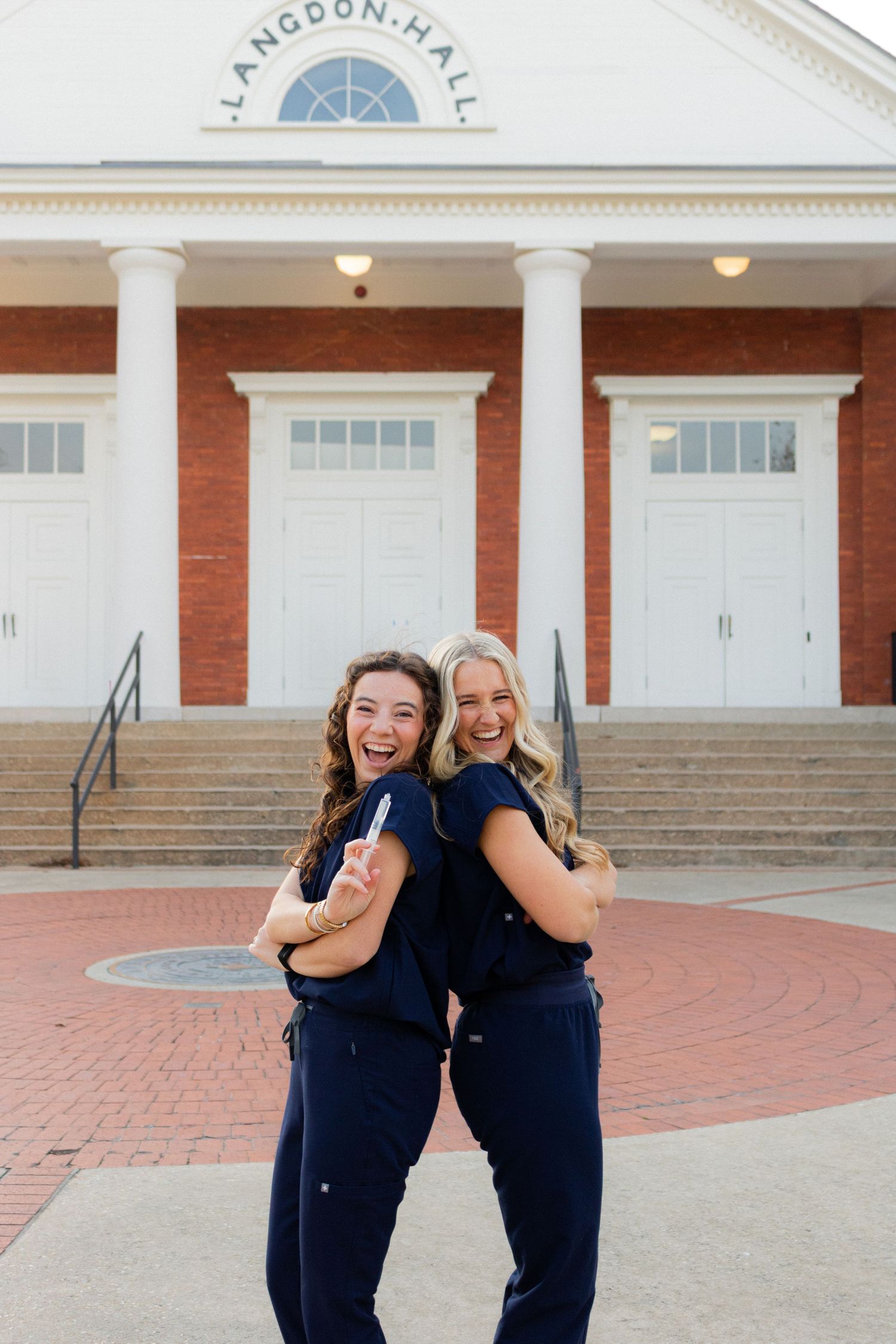 People in matching navy uniforms pose playfully in front of a brick building.