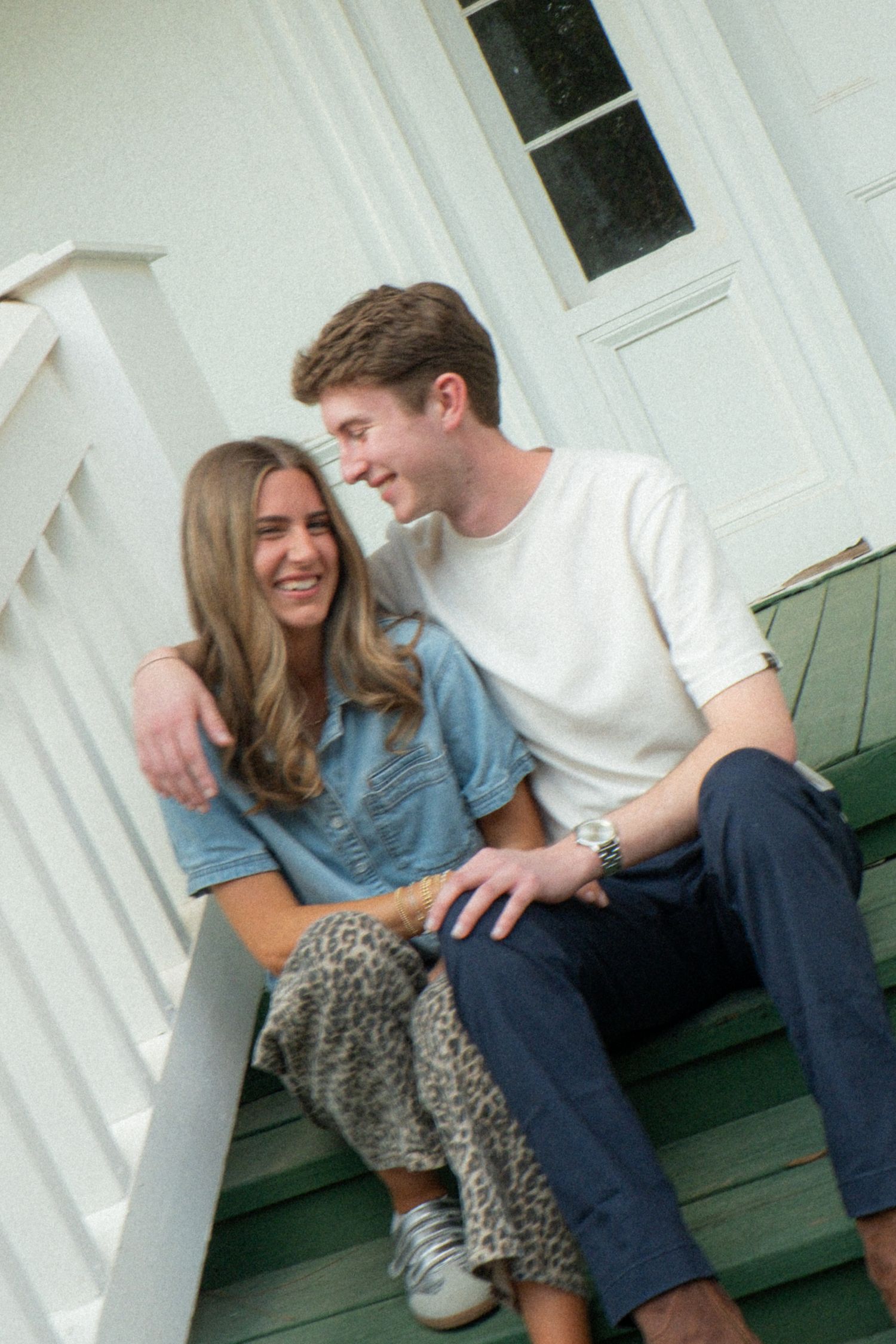 A couple shares a tender moment while sitting together on white porch steps.