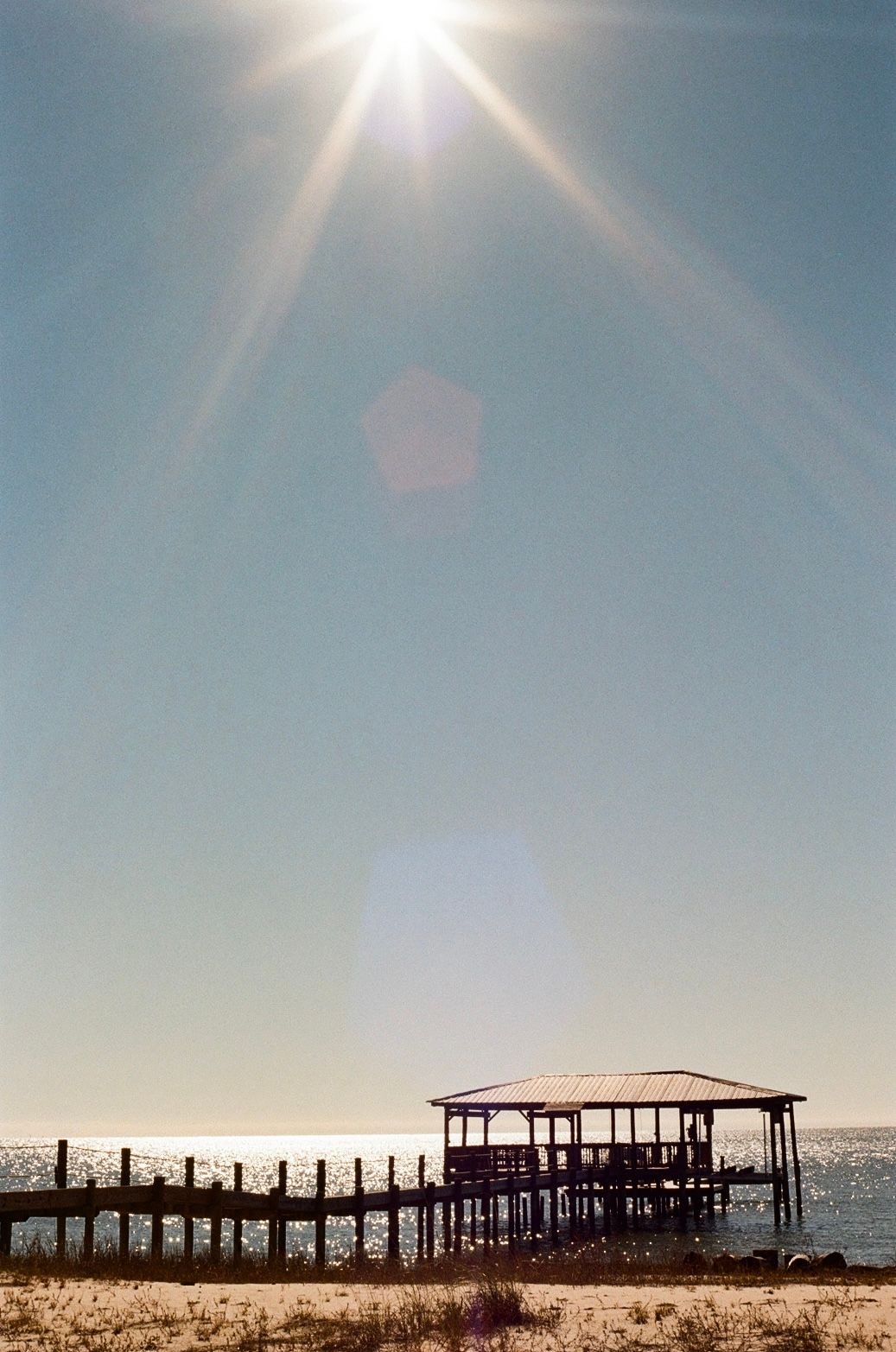 Wooden pier with covered dock extends into water under bright sunlight.