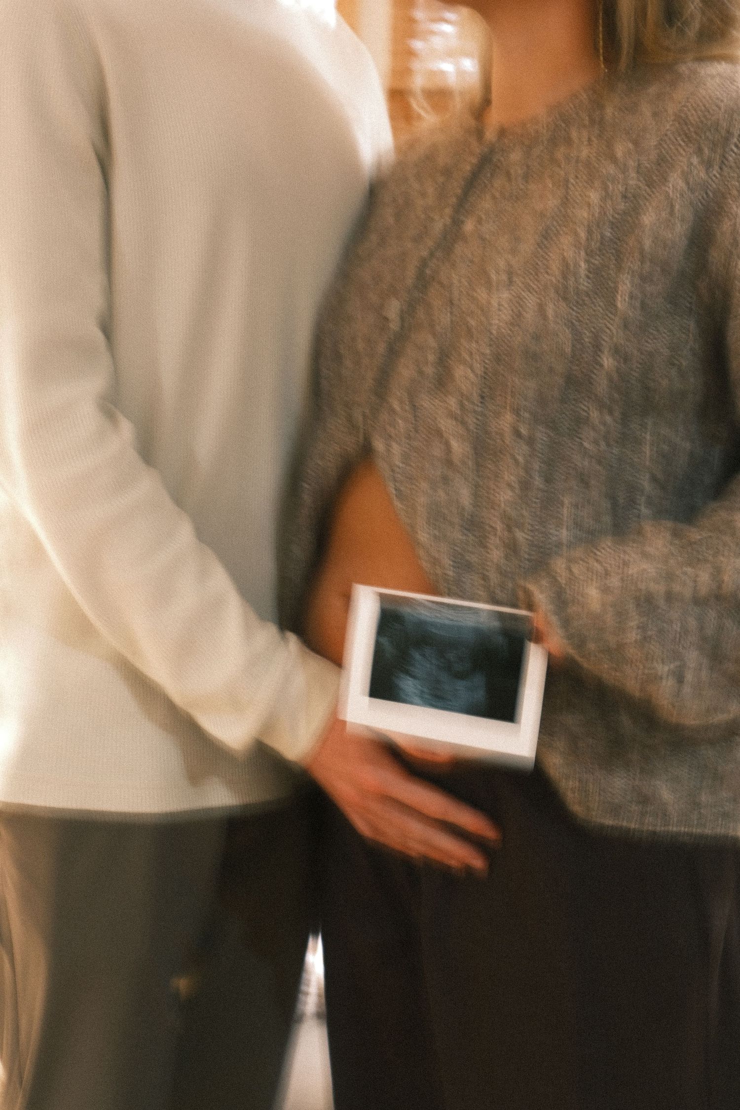 Two people hold an ultrasound photo together in a blurred intimate moment.