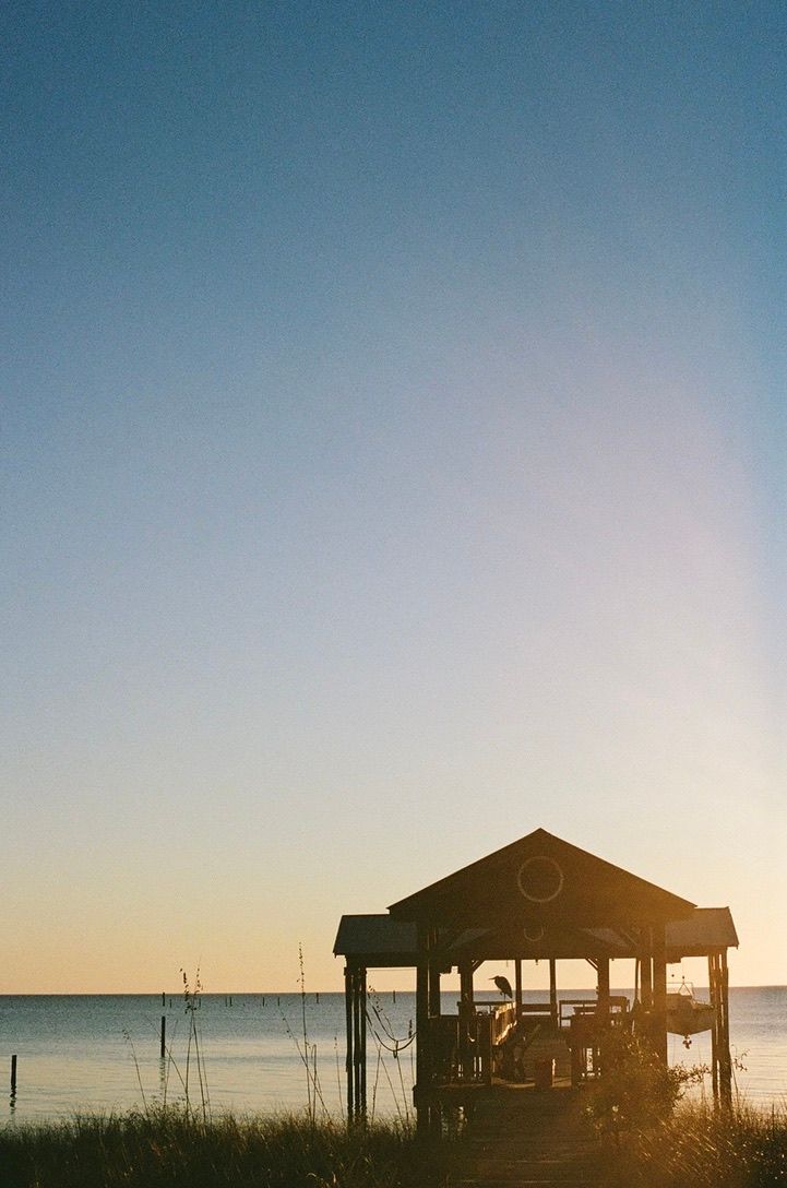 Silhouettes of beach houses stand against a vibrant sunset sky over the ocean.