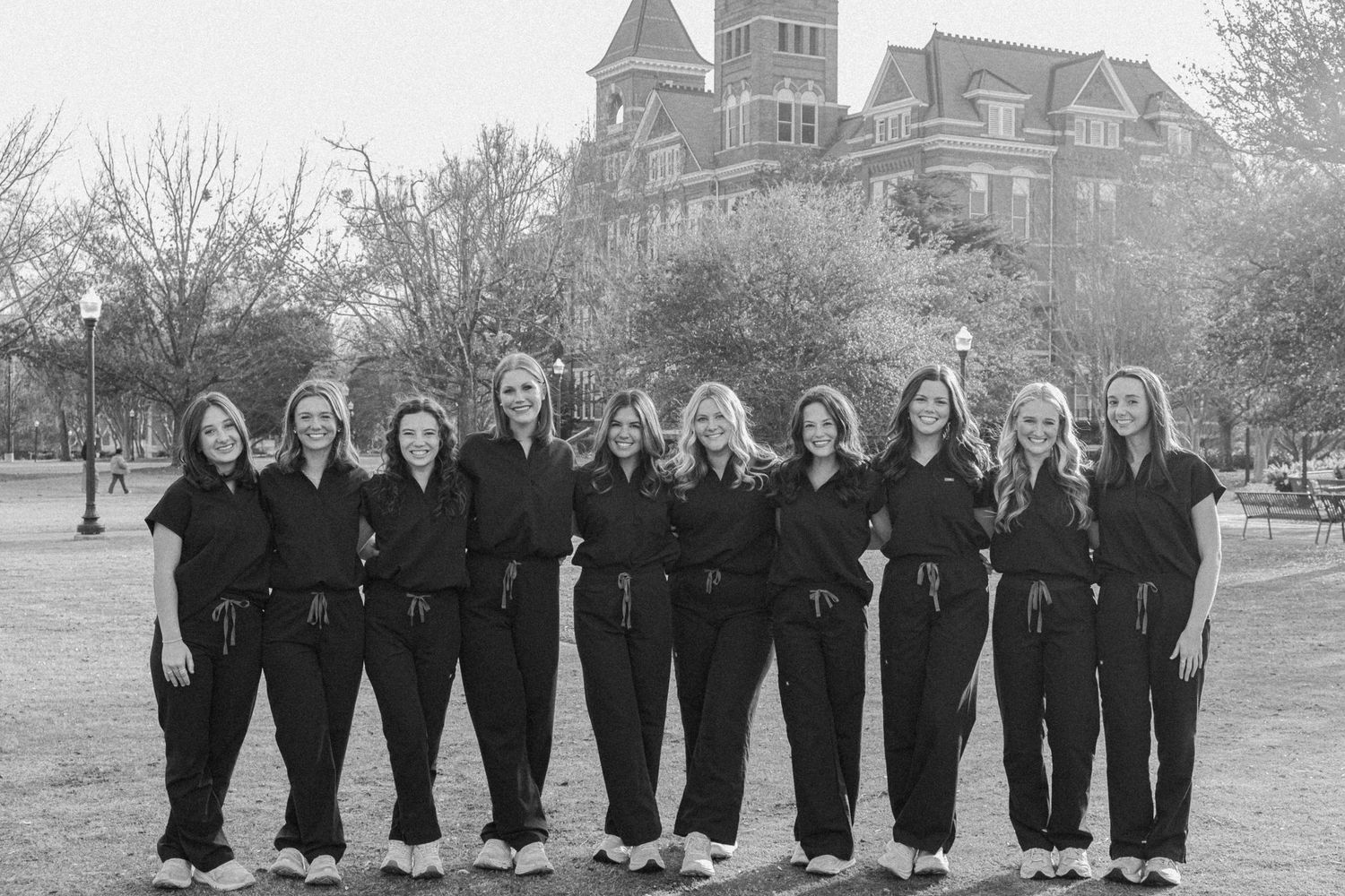 Group photo of people wearing matching dark outfits standing in front of a historic building.