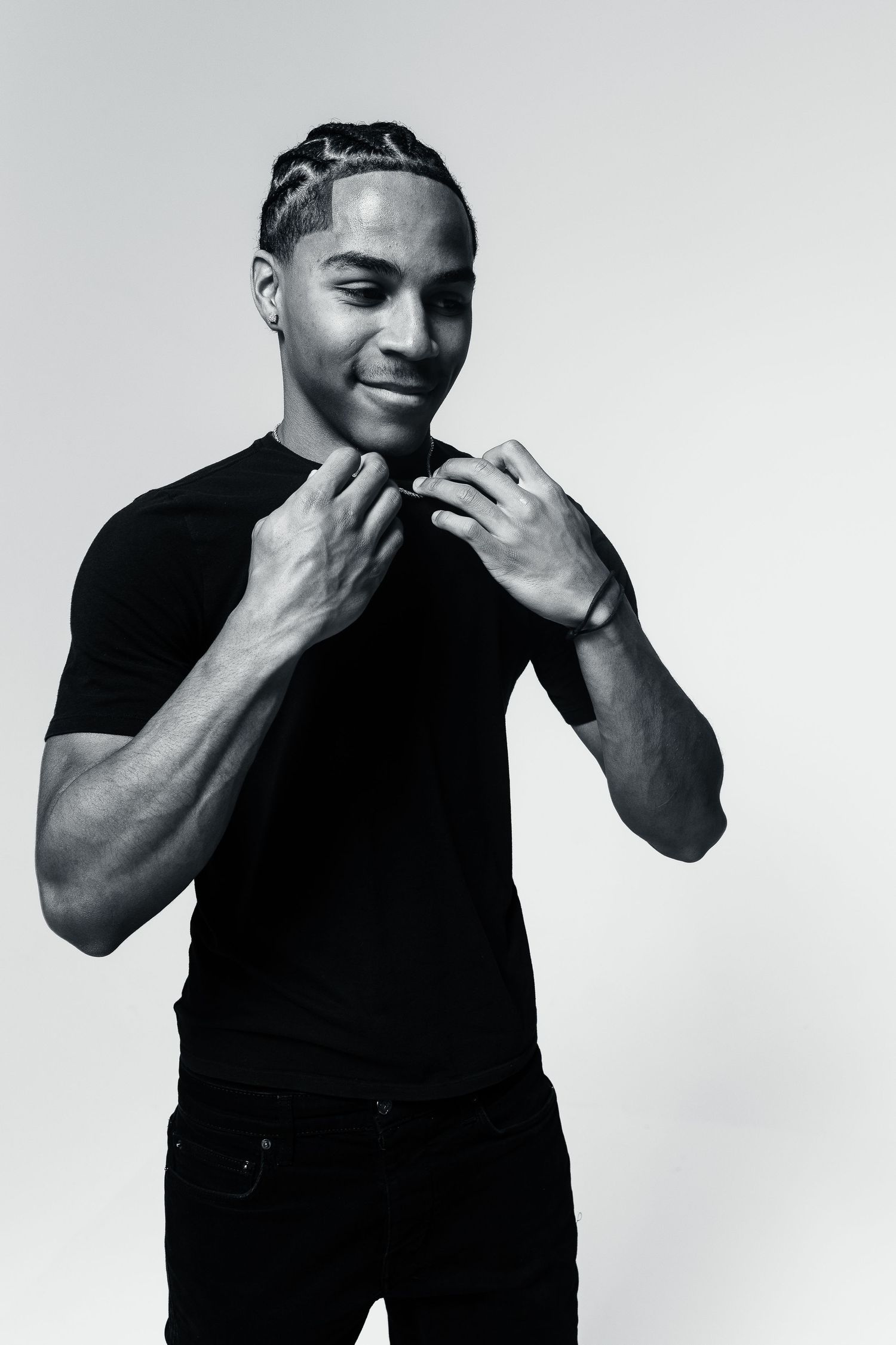 Black and white portrait of person in dark t-shirt and jeans posing with hands near chin against plain background.