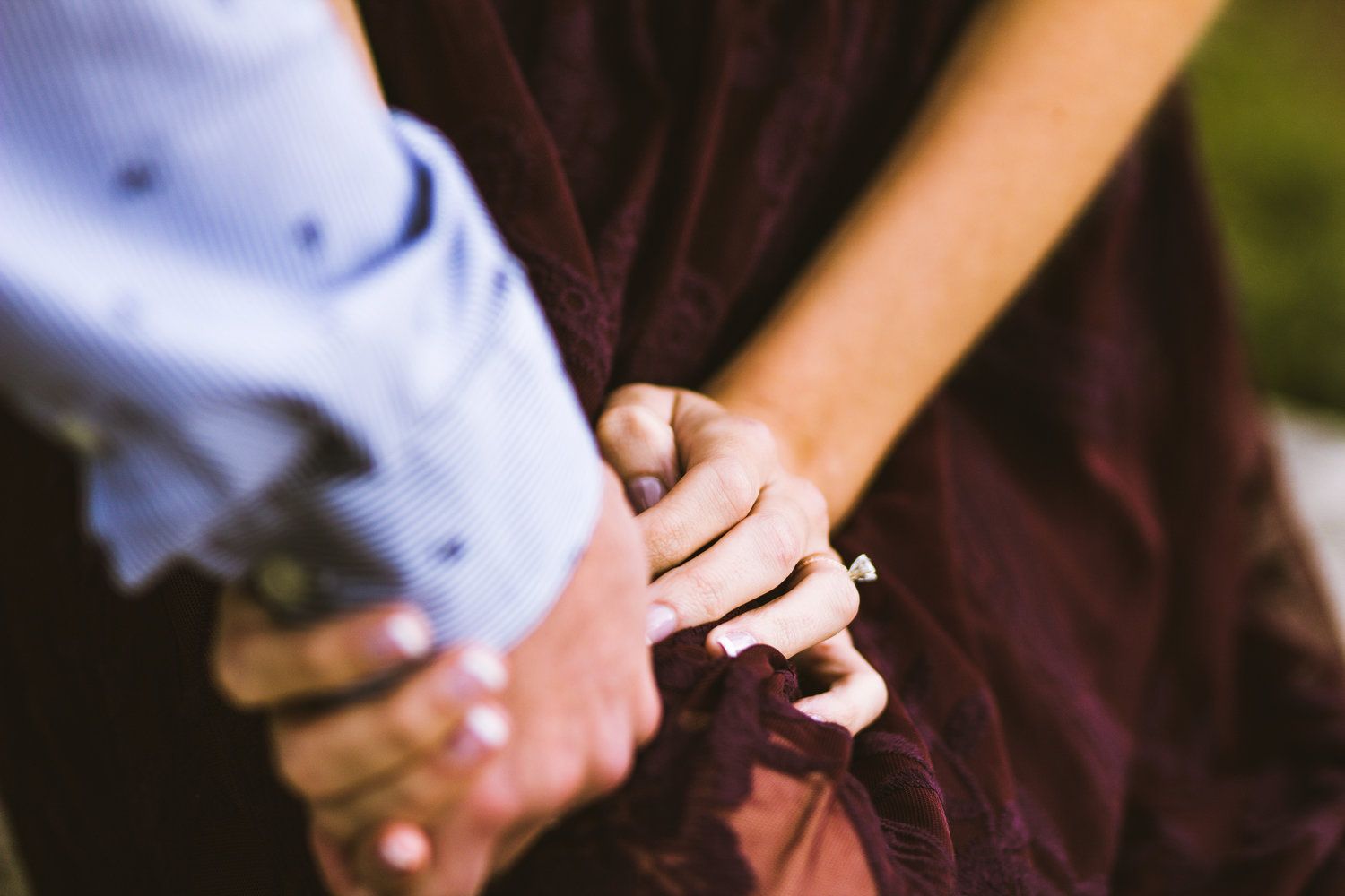 Close-up of hands exchanging wedding rings during an outdoor ceremony with natural lighting and greenery in background.