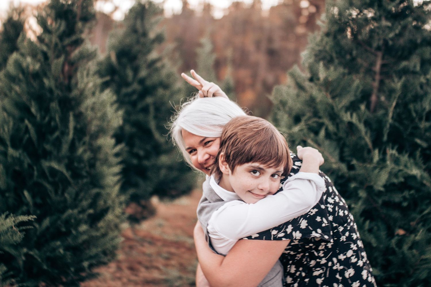 A couple embraces in a romantic moment among evergreen trees during a golden autumn sunset.
