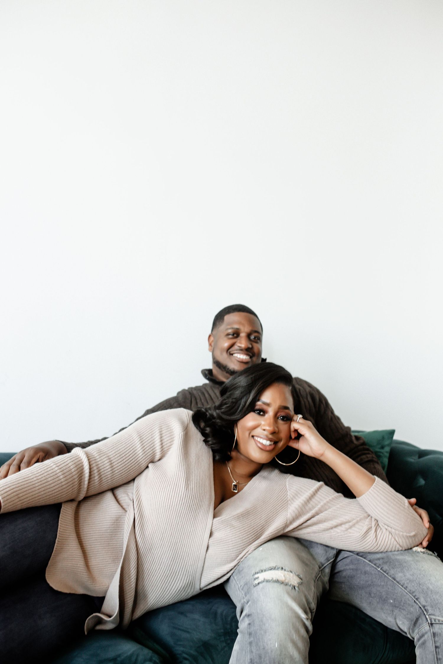 A couple relaxing together on a dark couch against a white wall.