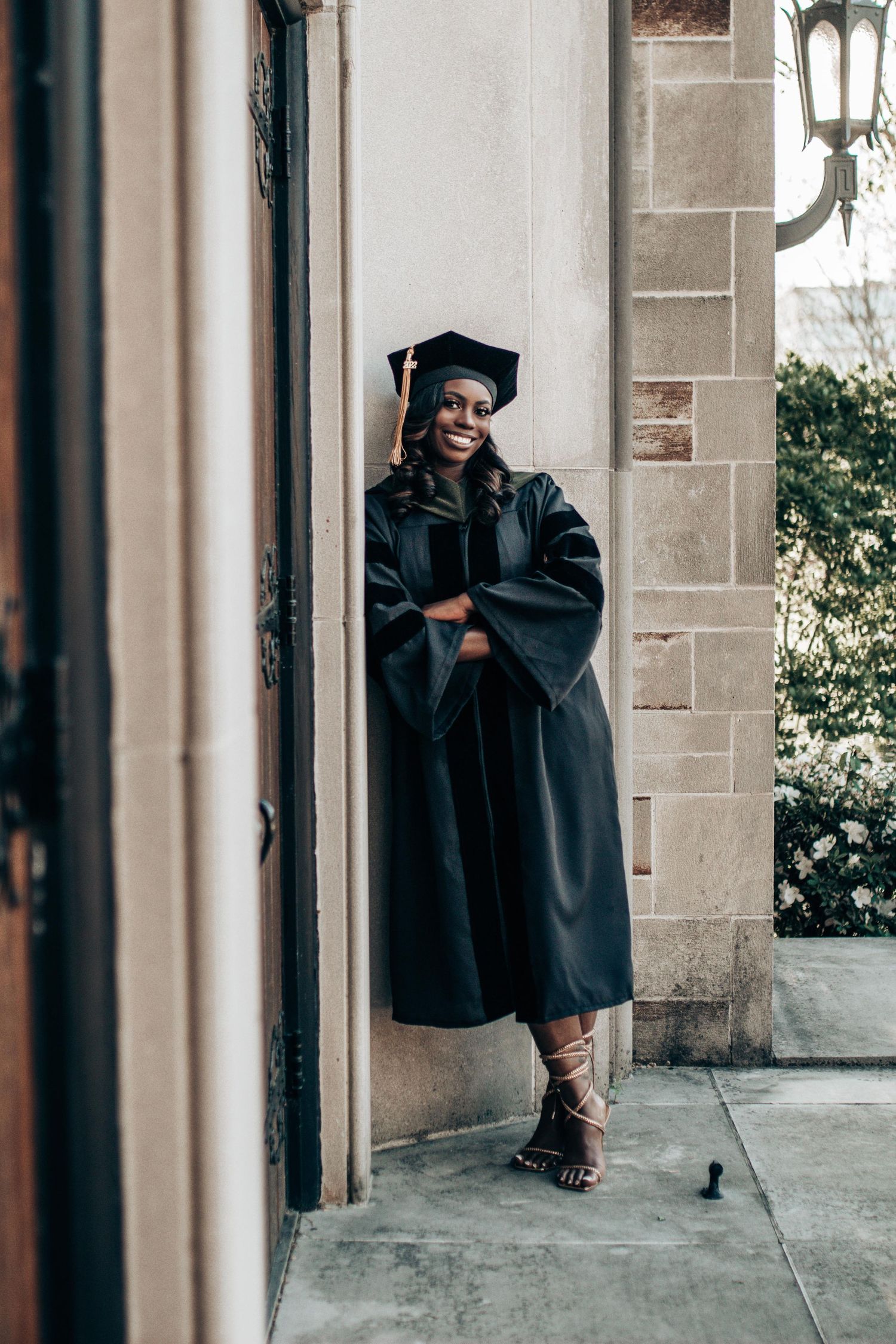 Graduate in black cap and gown poses in a series of artistic shots against stone columns and archways.