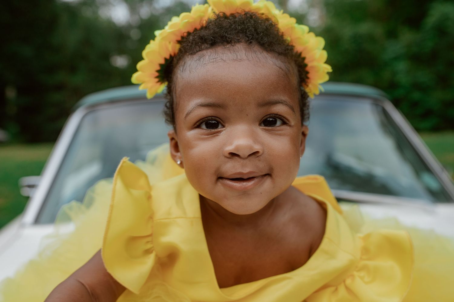 A bright yellow dress adorns a figure against a natural outdoor background with trees and cars visible.