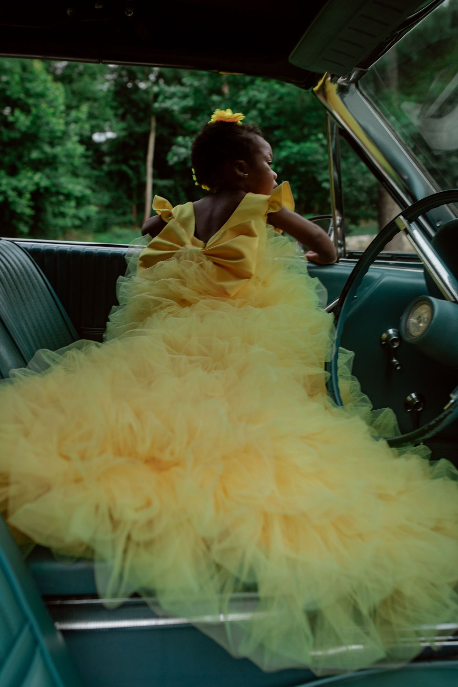 A voluminous yellow tulle dress fills the front seat of a car, creating a dramatic cloud-like effect against the interior.
