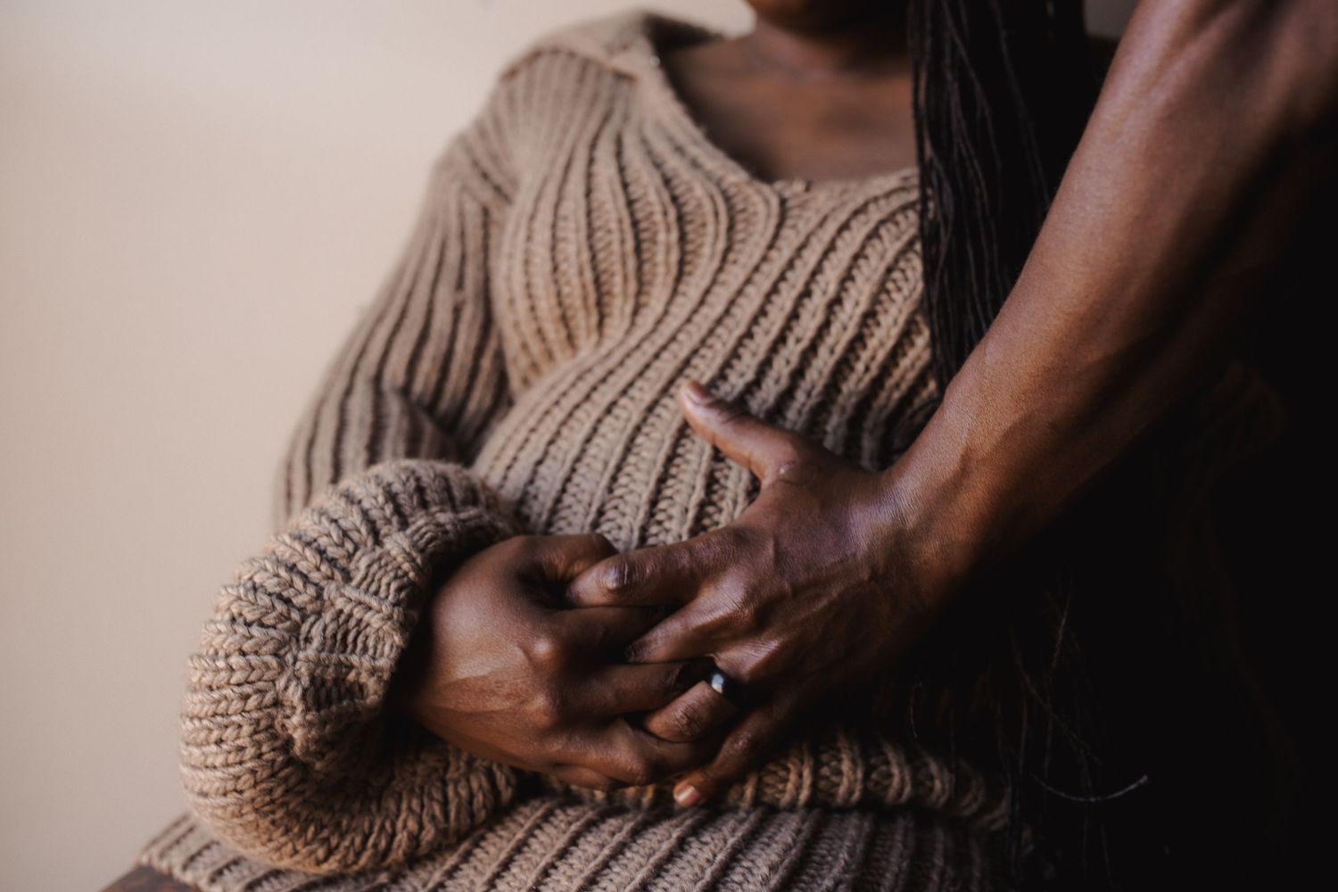 Close up shot of hands braiding cornrows in dark hair against a neutral background.