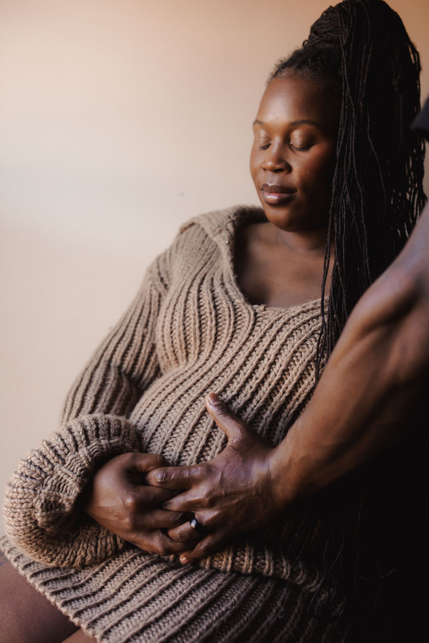 Artistic portrait series showing hands gently cradling a beige knit sweater against dark skin in warm lighting.