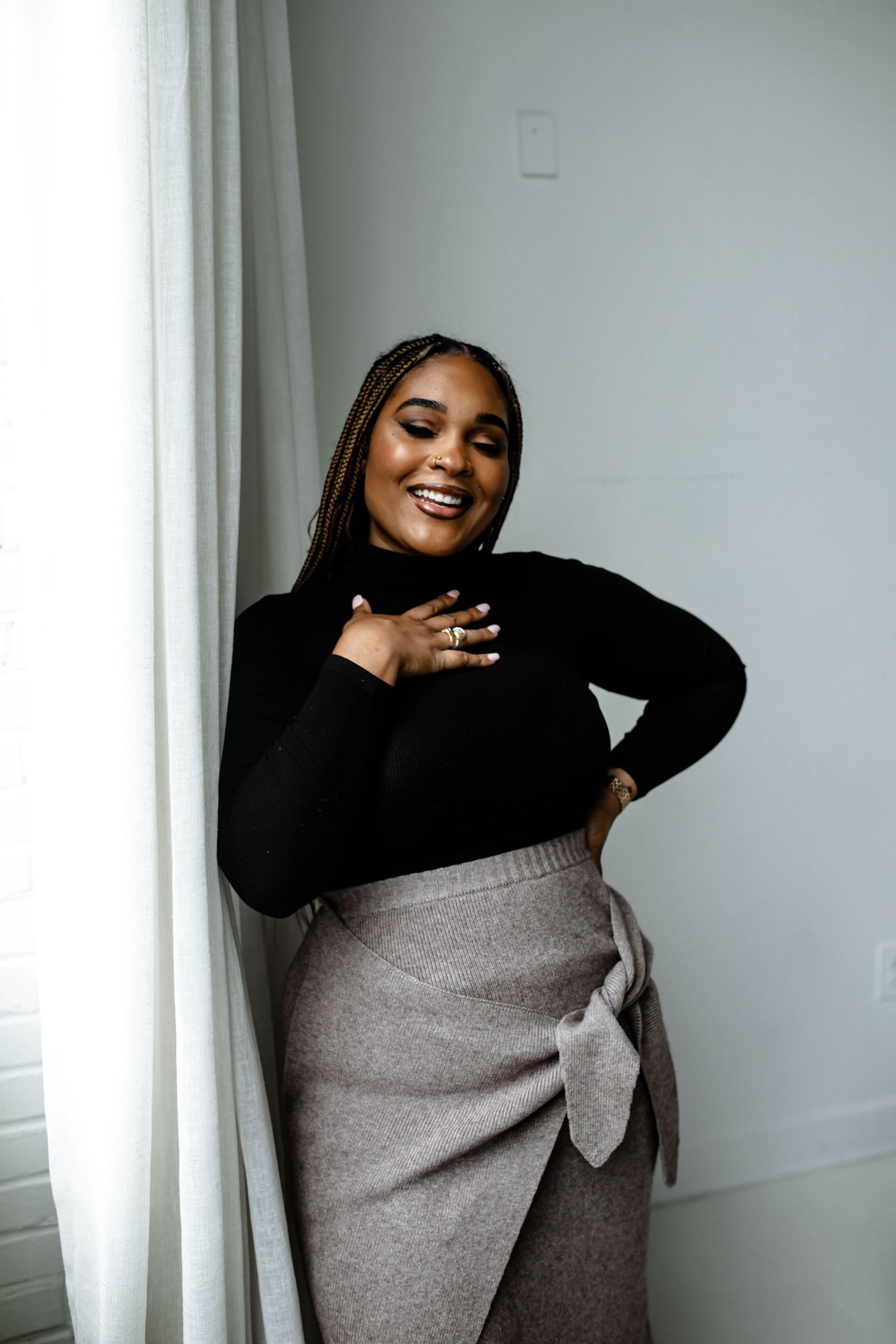 A person in a black top and gray skirt poses playfully against a white wall in a three-panel photo series.