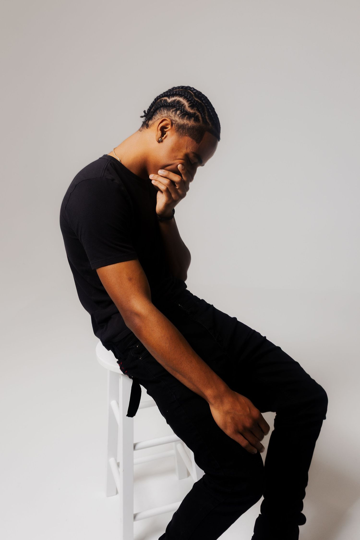 Model in all black attire poses on white chair showing different angles in studio photoshoot.