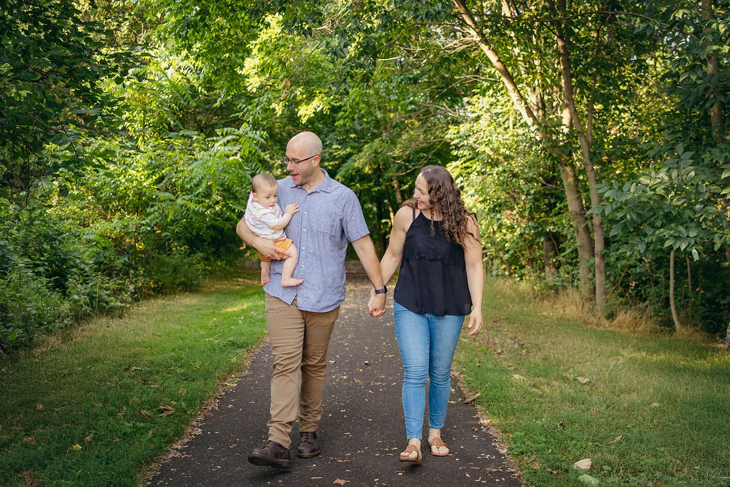 Family walking together on a tree-lined path during a sunny afternoon.