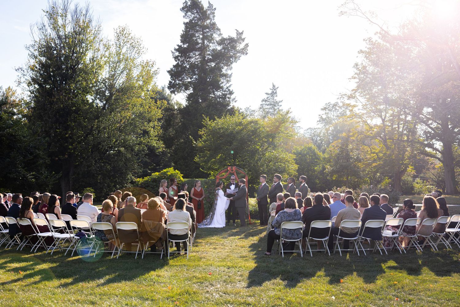Outdoor wedding ceremony setup with chairs facing wooded area in natural sunlight.