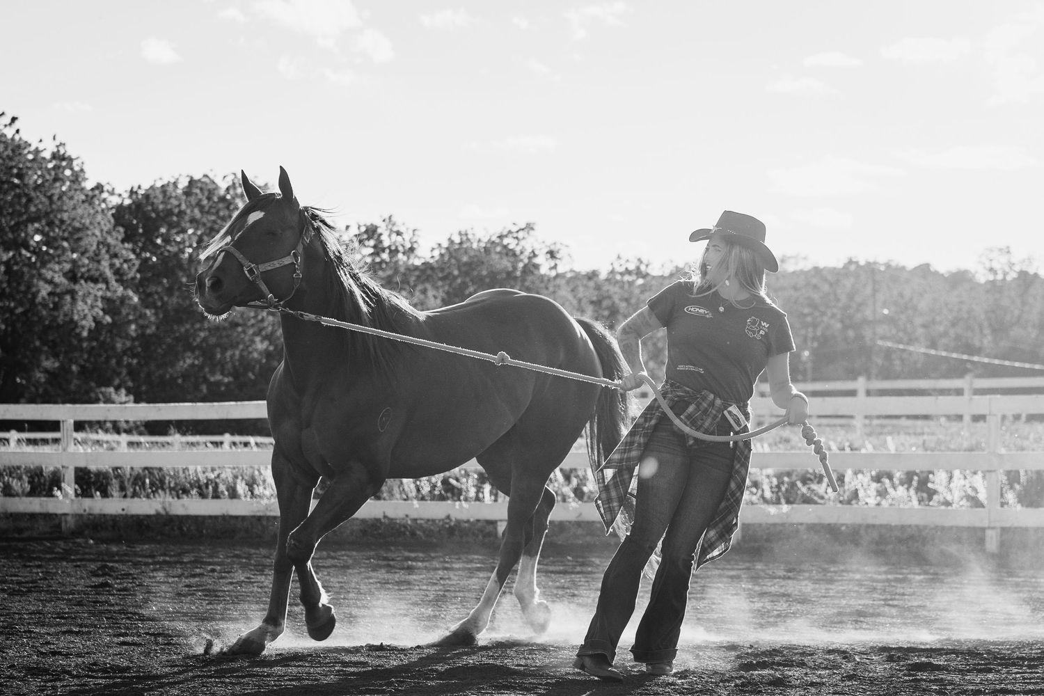 Black and white photo of a cowgirl leading a horse in a dusty rodeo arena with spectators in the background.