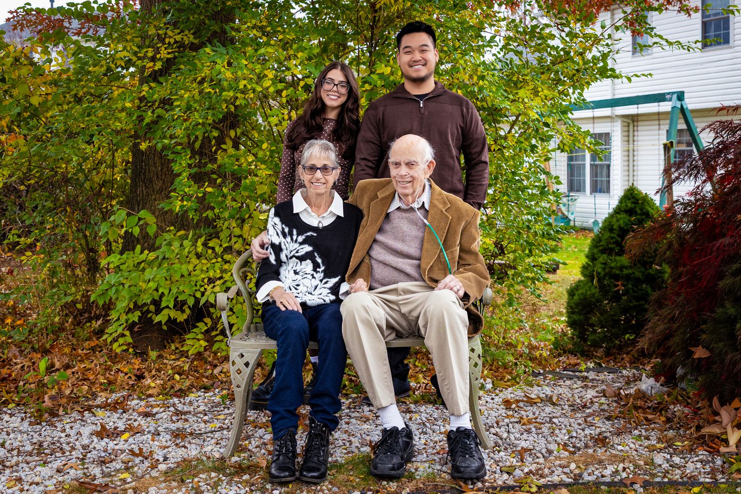 Family sitting together on fallen autumn leaves in front of a white house.