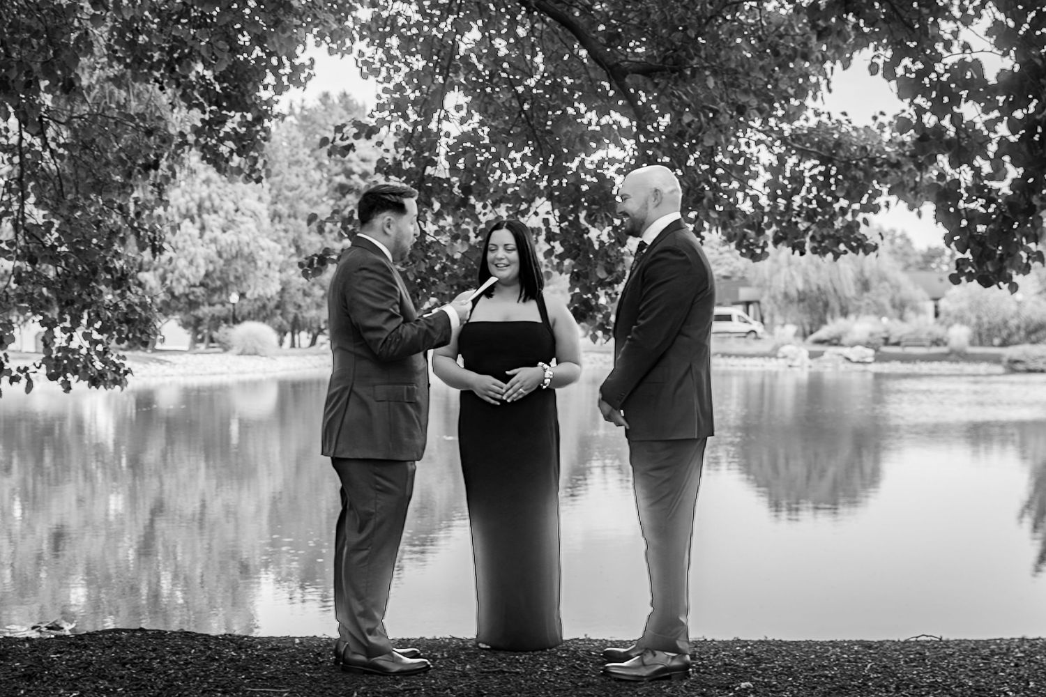 Black and white lakeside ceremony photos with trees and water in the background.