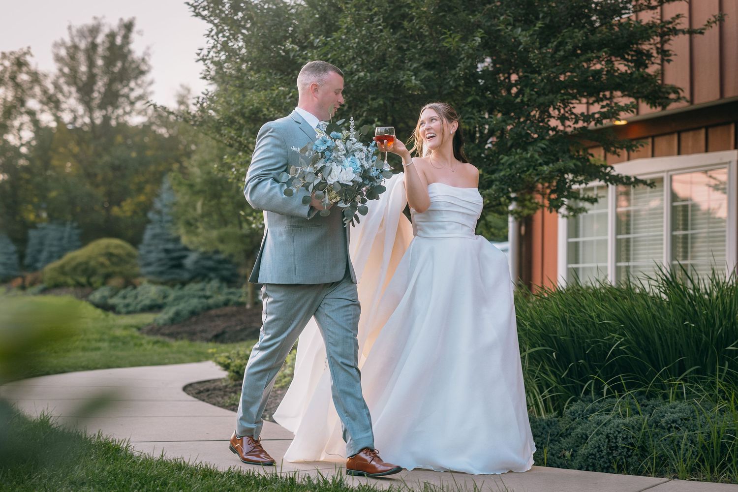 Wedding couple poses outside rustic brown wooden building surrounded by greenery.