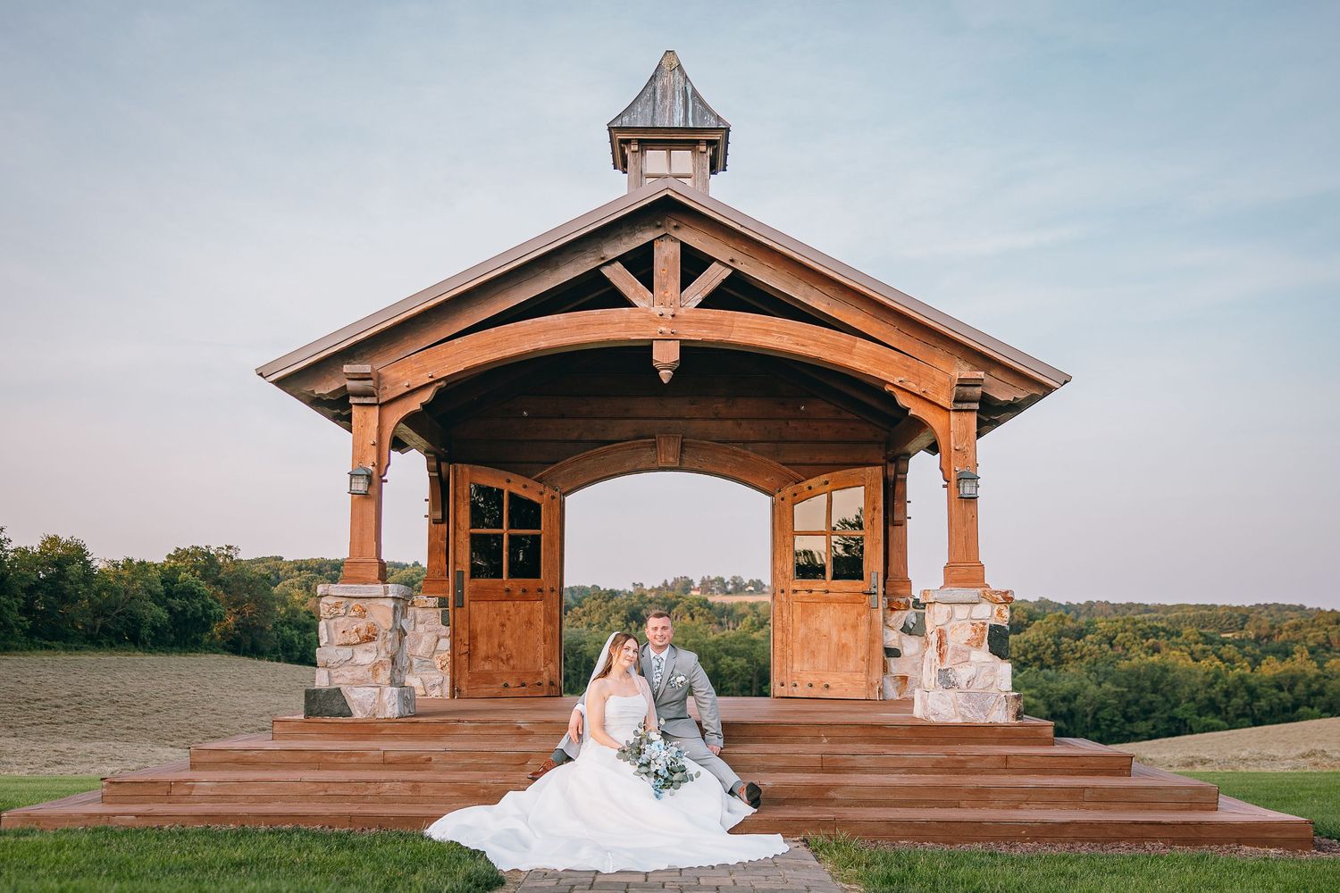 Rustic wooden wedding chapel with stone pillars against a blue sky.