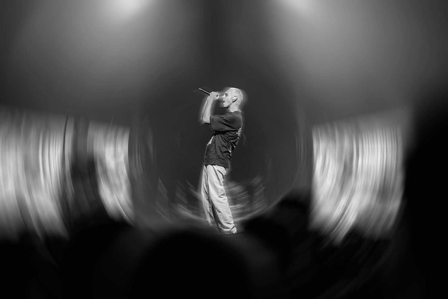 Black and white photo of a performer singing on stage with dramatic lighting and motion blur effect.