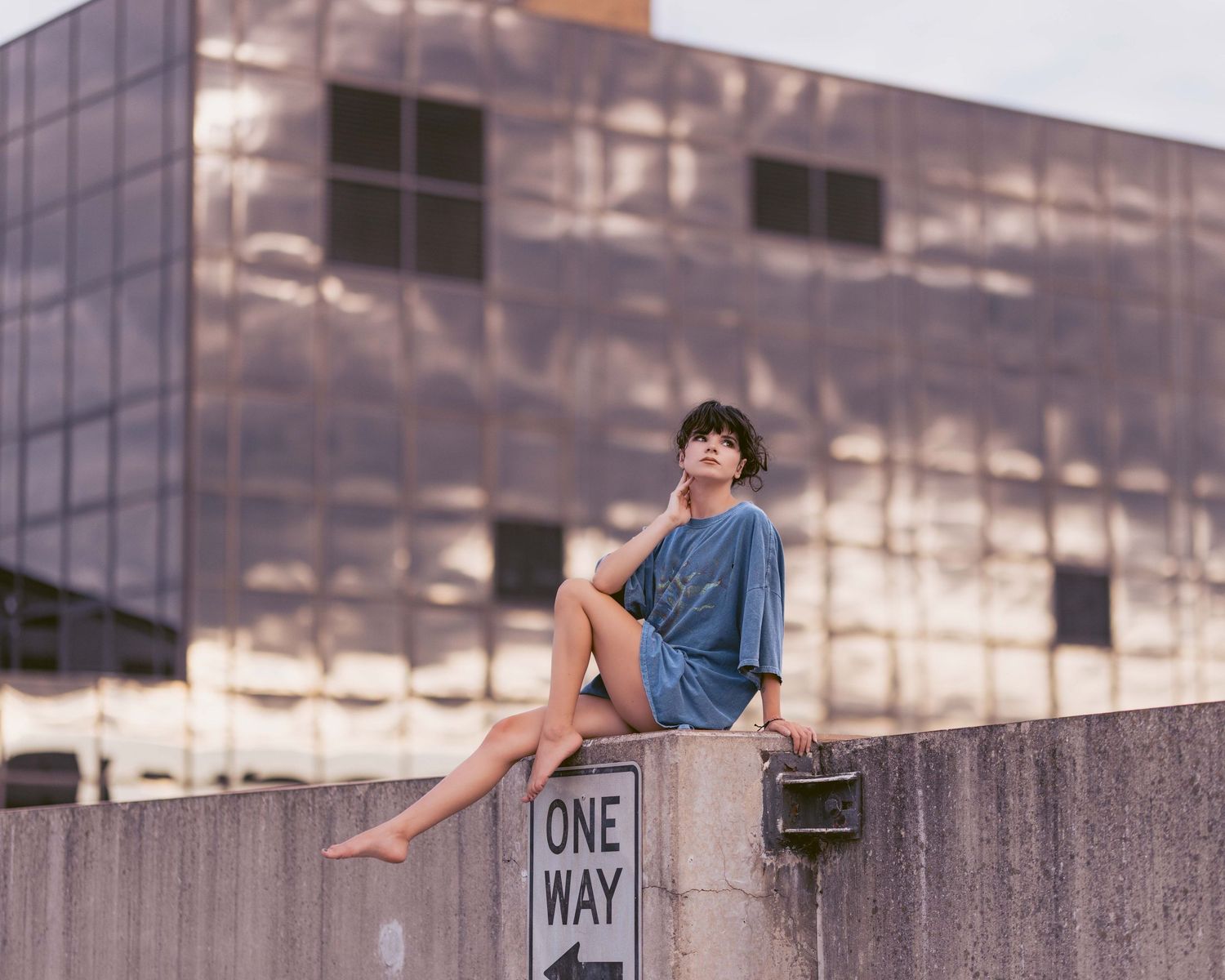 Person sitting casually on concrete wall of urban building.