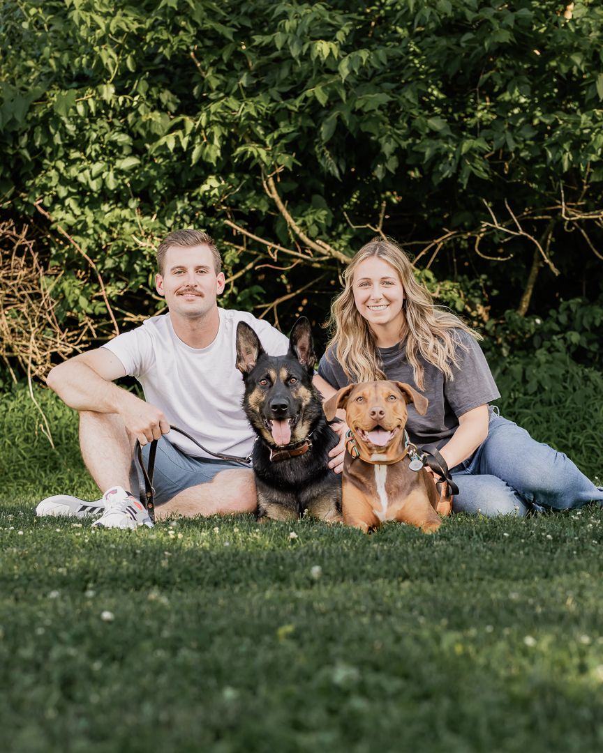 Family lounging on grass with their three dogs in a garden setting.
