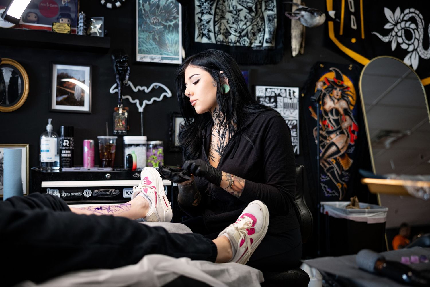 Dark tattoo studio interior with artwork and equipment on black walls.