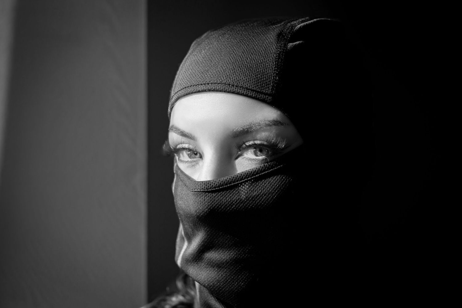 Black and white portrait of a person wearing a black balaclava mask, with intense eyes visible.