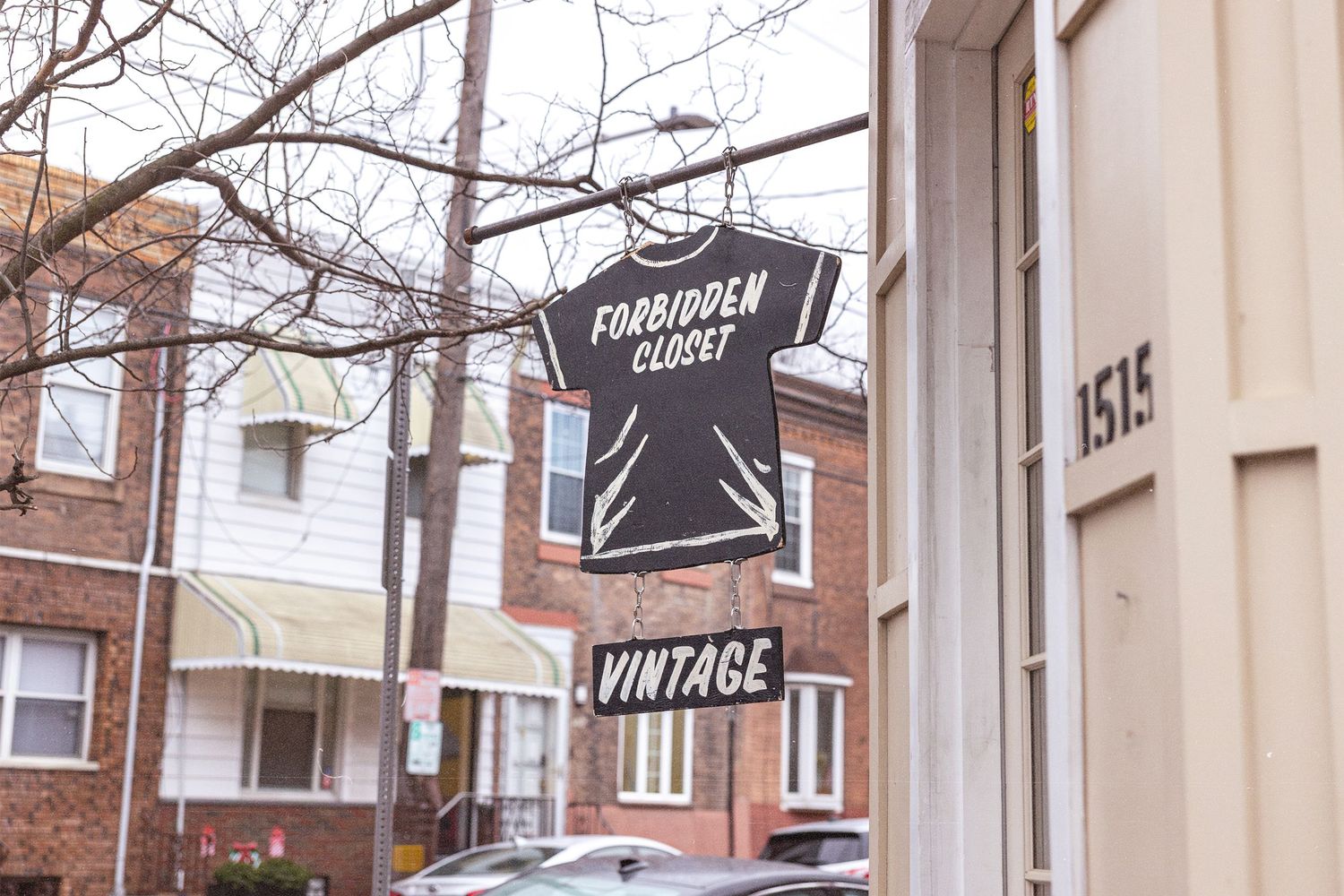Forbidden Closet Vintage shop sign shaped like a t-shirt hanging outside a brick building at address 1515.
