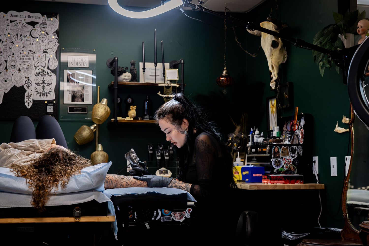Professional tattoo artist working on a client's arm in a dark studio setting.