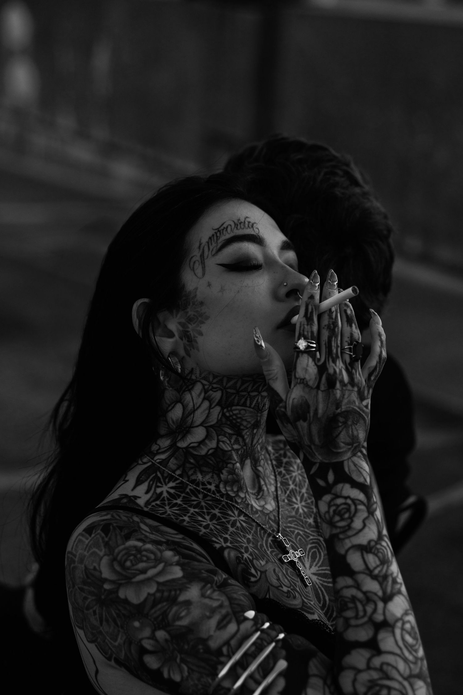 Person with elaborate floral tattoos and dark hair in dramatic lighting.