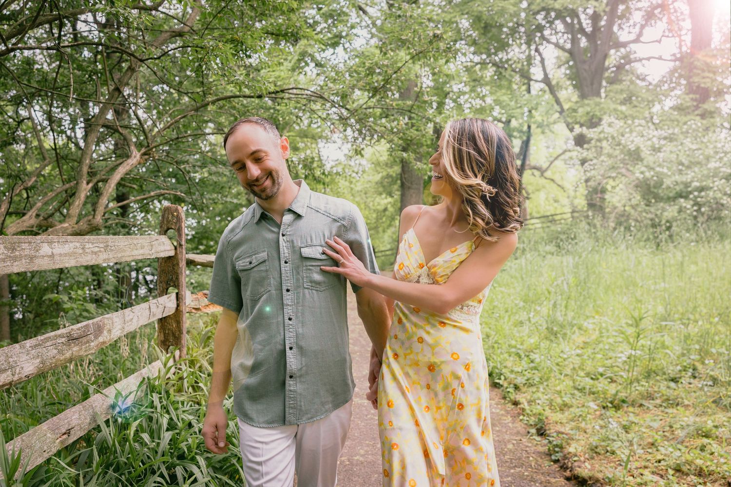 Couple walking on a garden path, man in green shirt and woman in yellow floral dress, smiling outdoors.