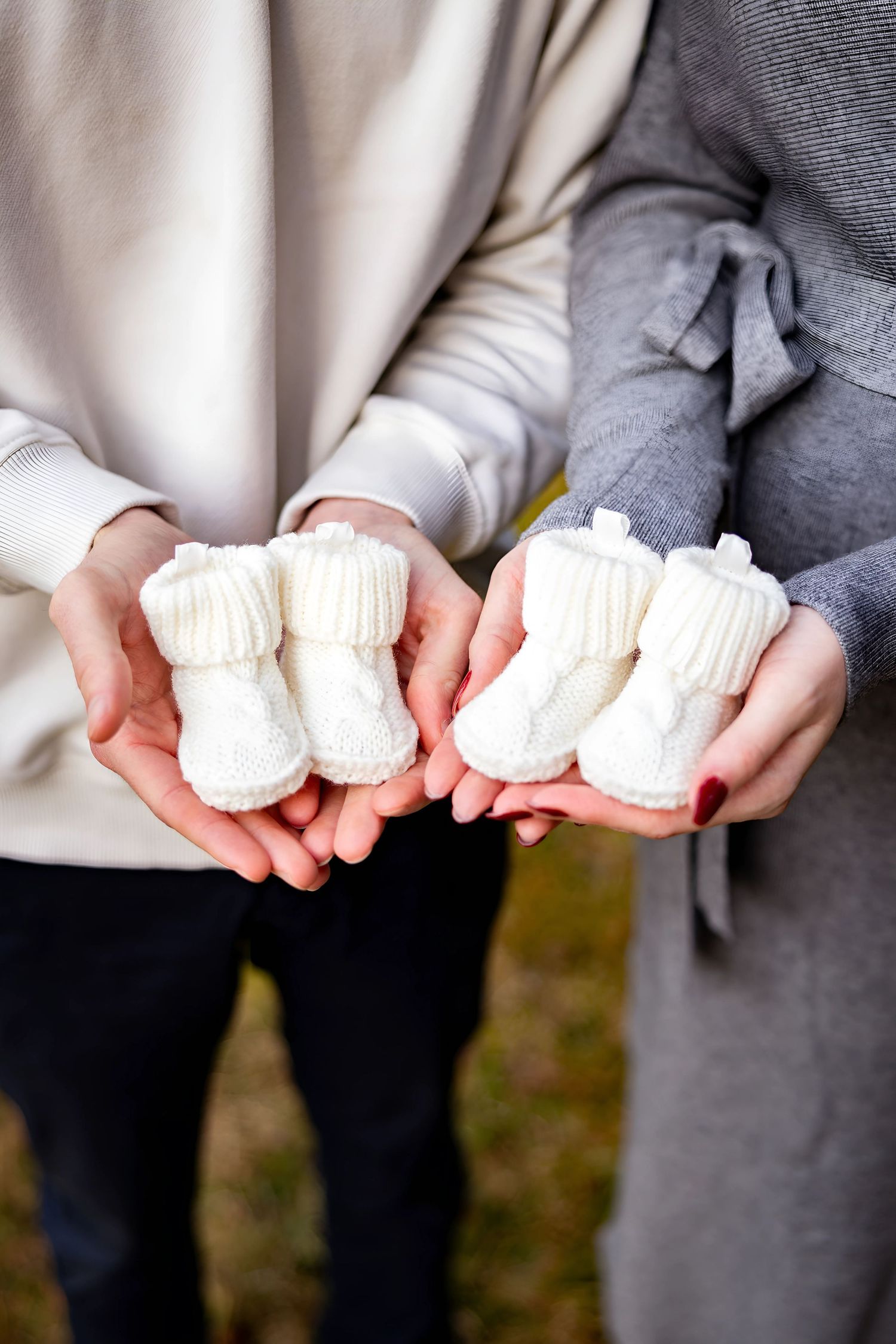 Hands holding small white knit baby booties in sequence.